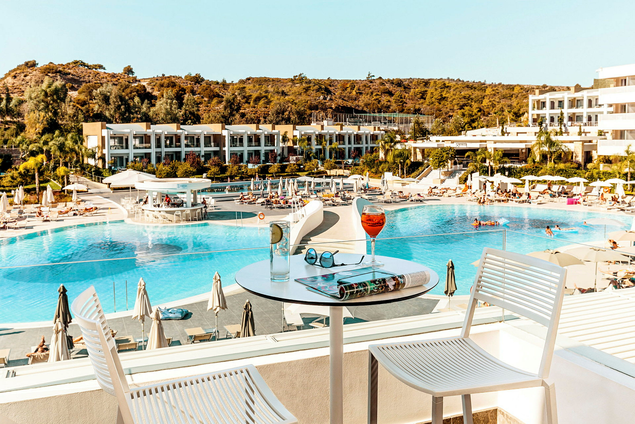 Hotellets poolområde med utsikt från en terrass med drycker på ett bord. (AI-genererad text)