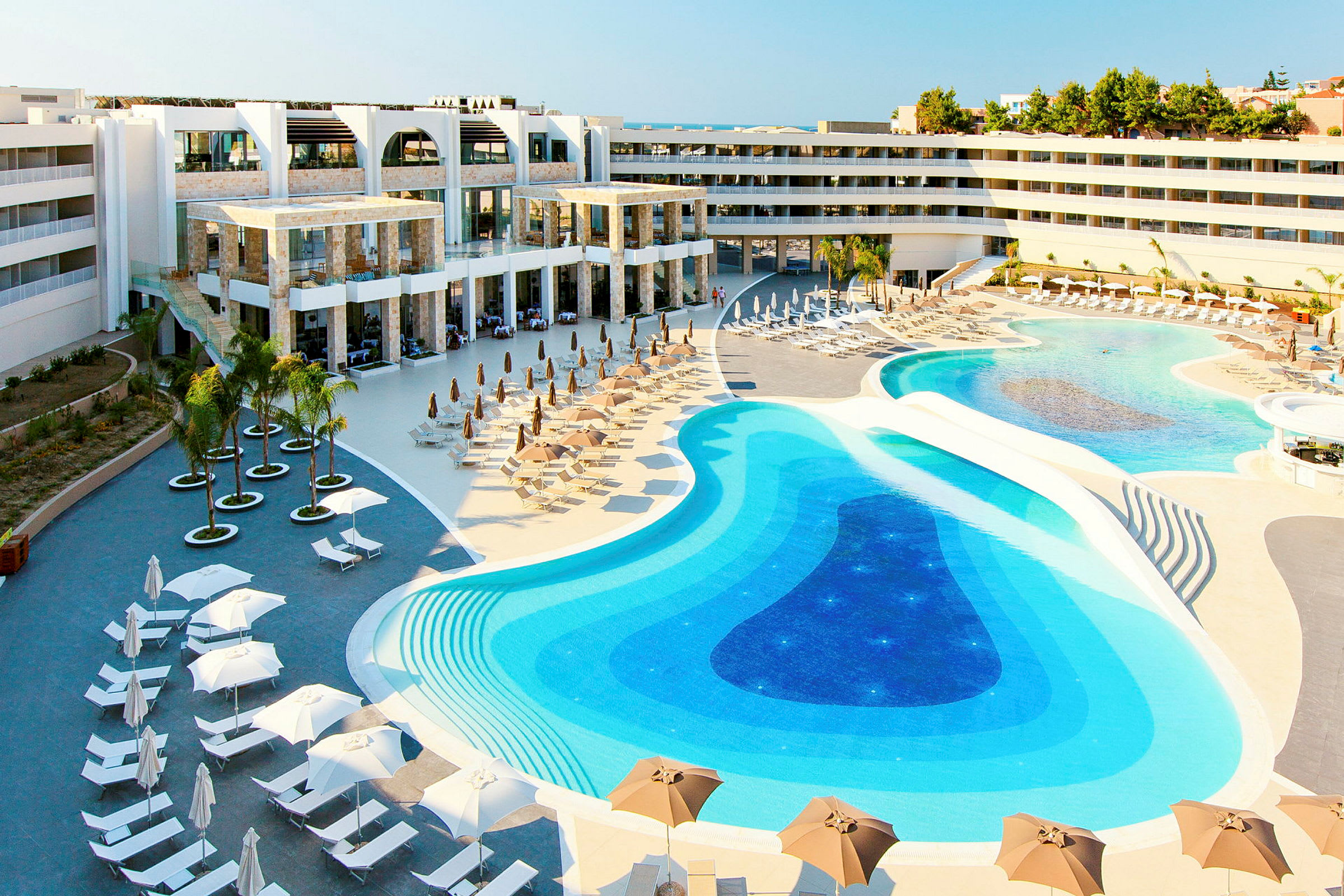Ett hotellområde med stora pooler och solstolar under parasoller. (AI-genererad text)