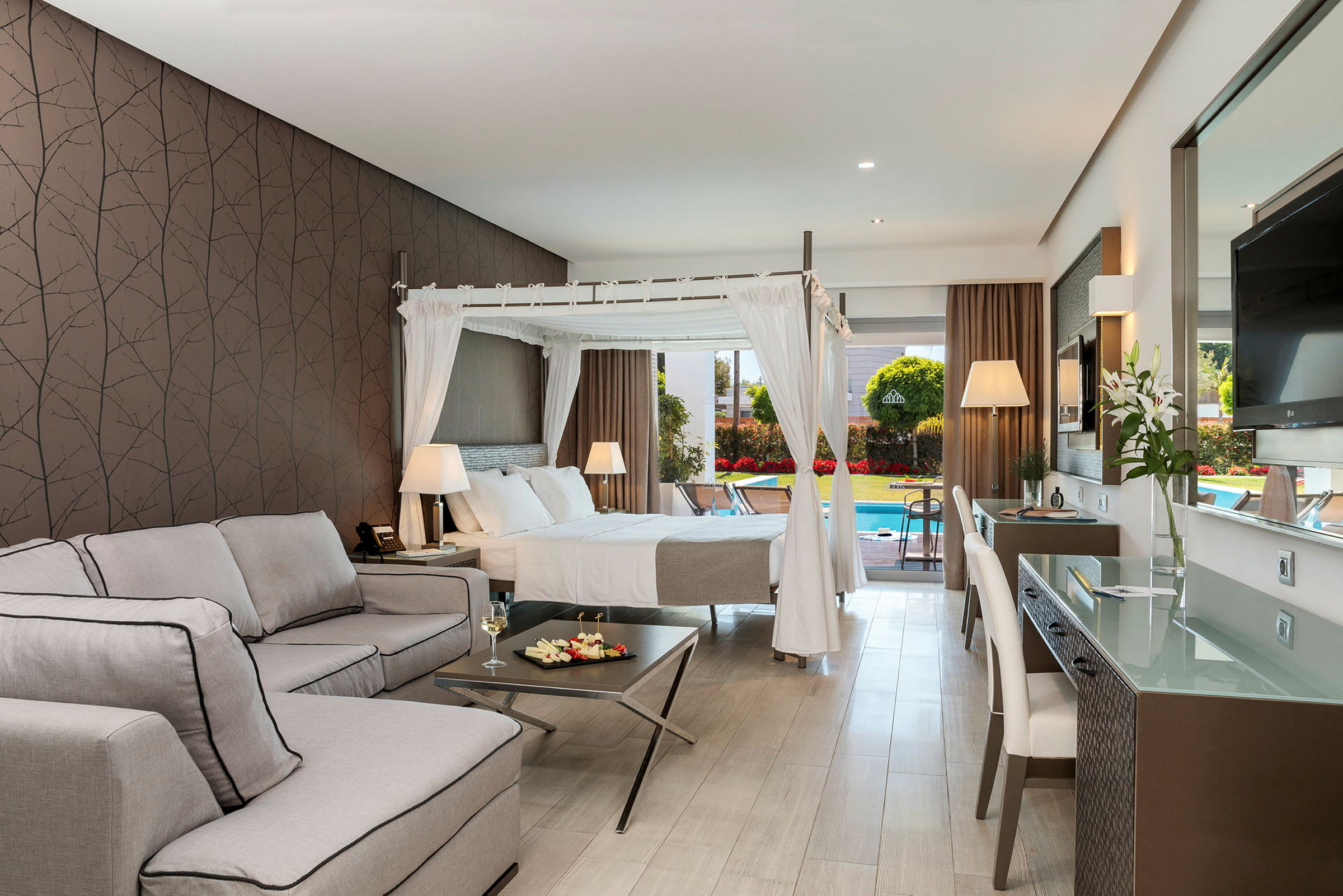 Hotellrum med himmelssäng och sittgrupp, samt utsikt mot poolområde. (AI-genererad text)
