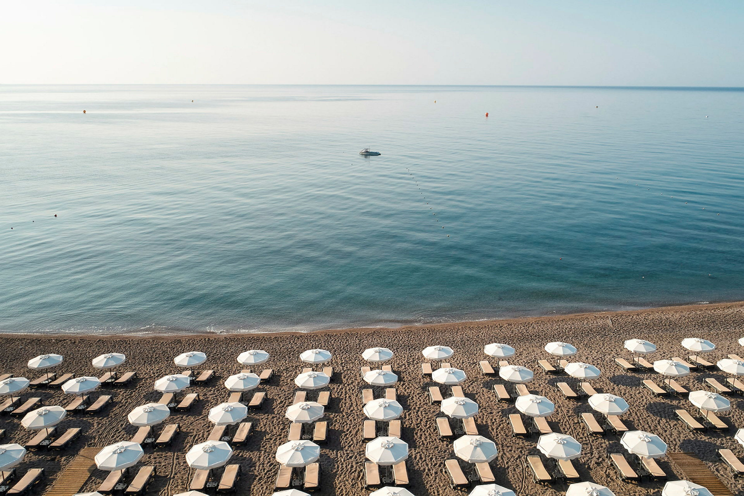 Strand med uppradade solstolar och parasoller, havet syns i bakgrunden. (AI-genererad text)
