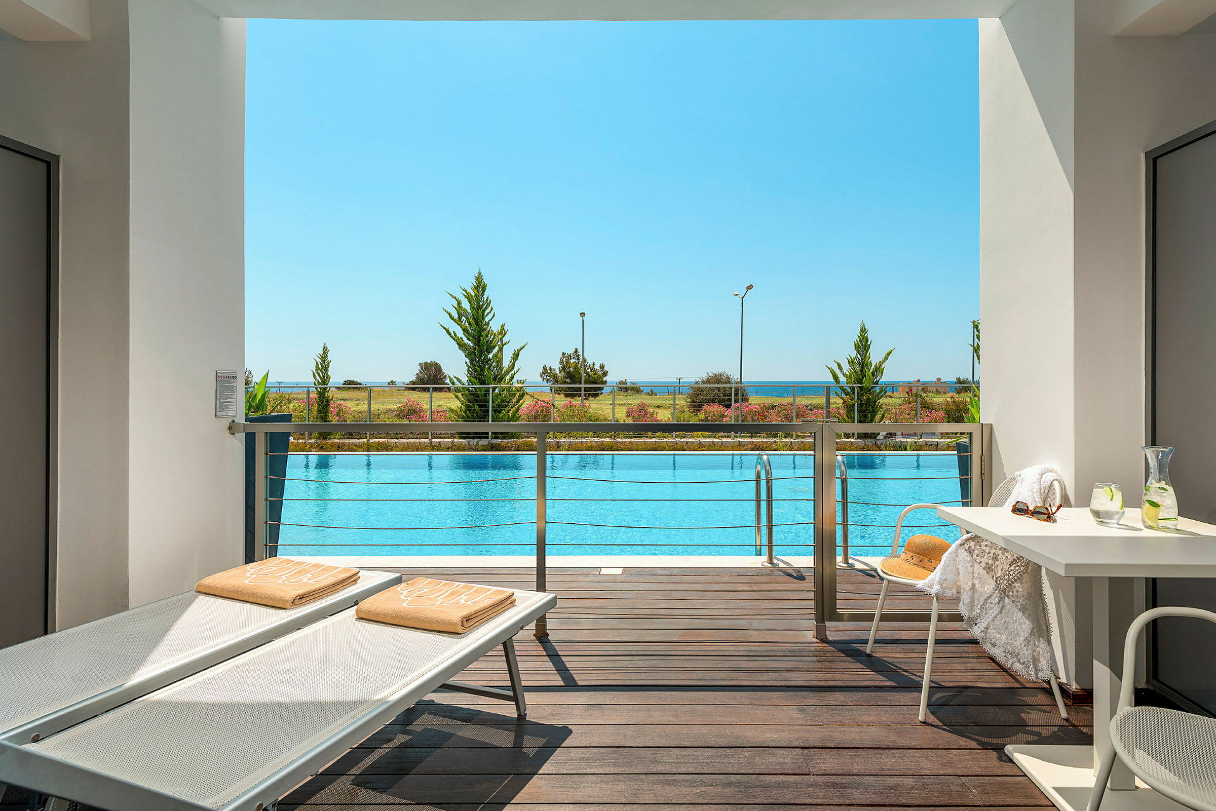 Utsikt från terrass över en pool, med strand och hav i bakgrunden. (AI-genererad text)