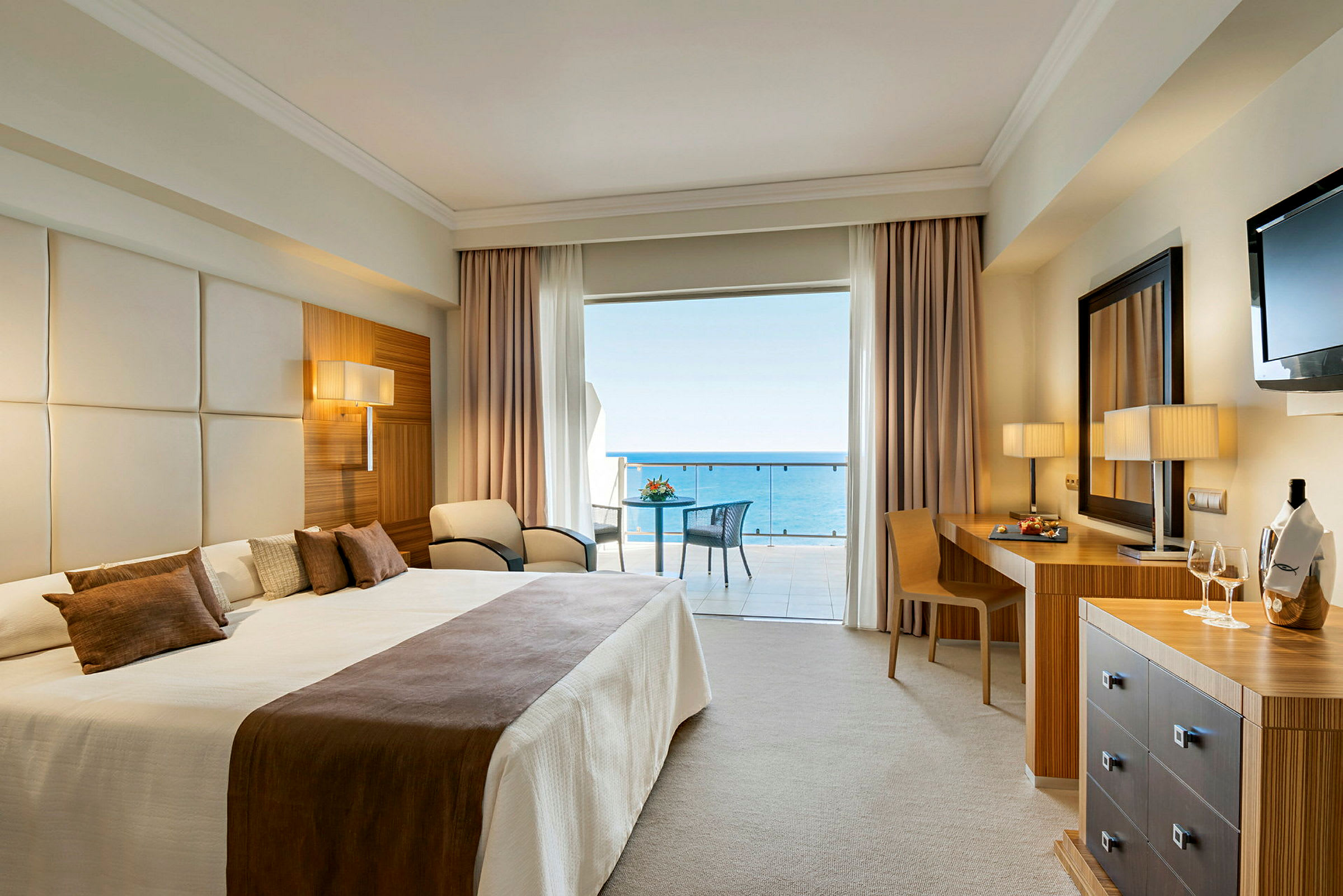 Hotellrum med stor dubbelsäng och utsikt mot havet från balkongen. (AI-genererad text)