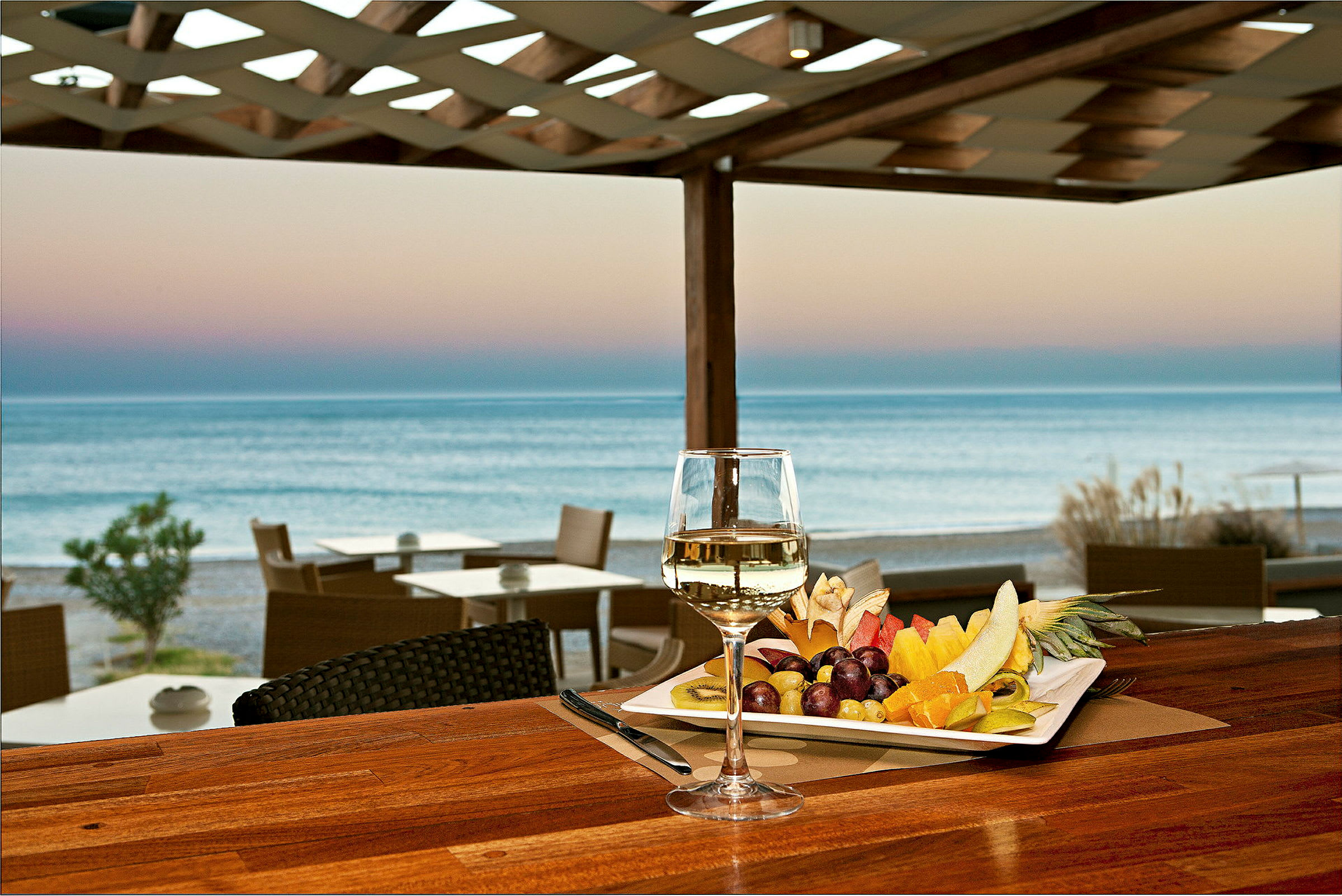 En tallrik med färsk frukt och ett glas vitt vin står på ett bord med utsikt över havet. (AI-genererad text)