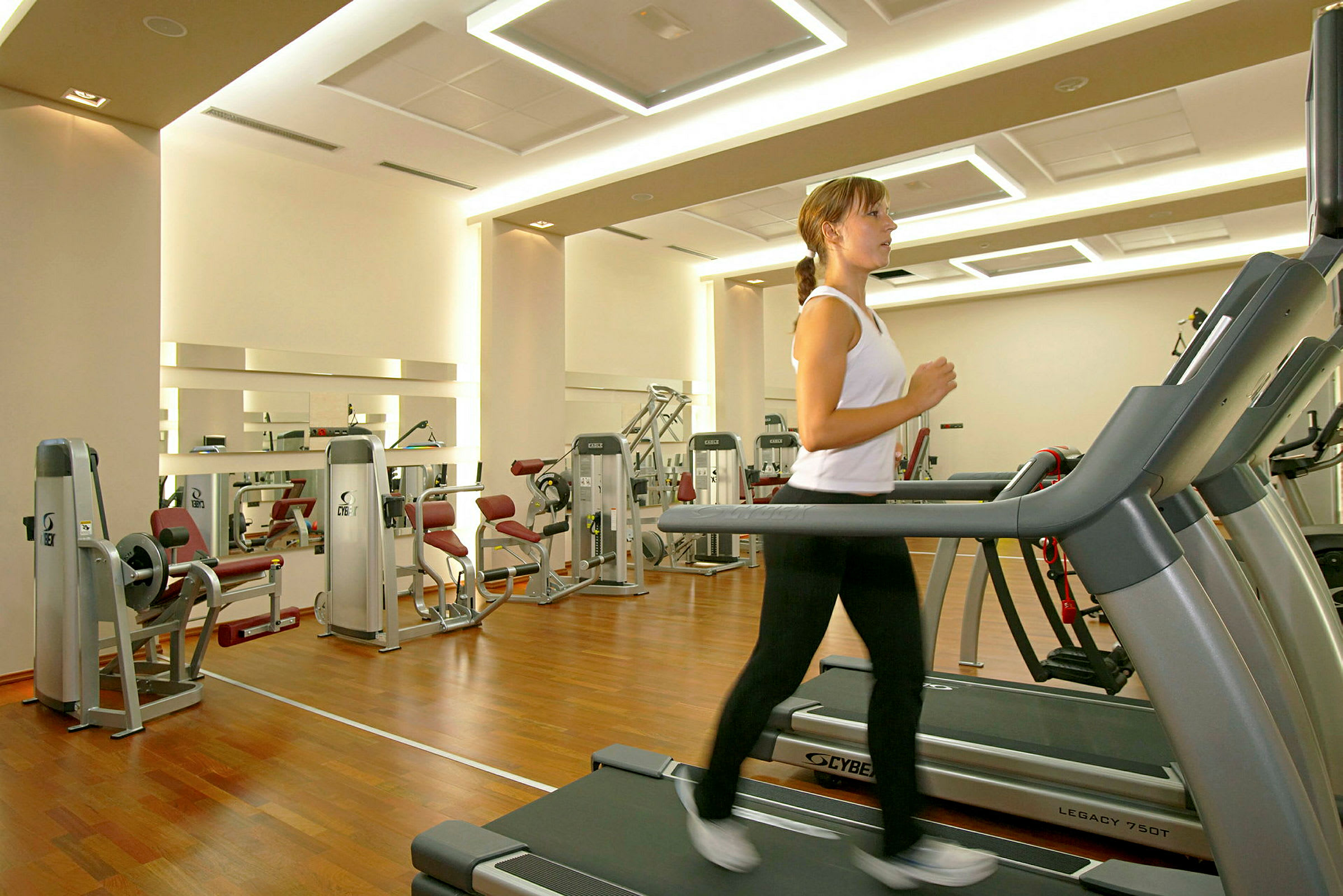 Gym med träningsutrustning och en person som springer på ett löpband. (AI-genererad text)