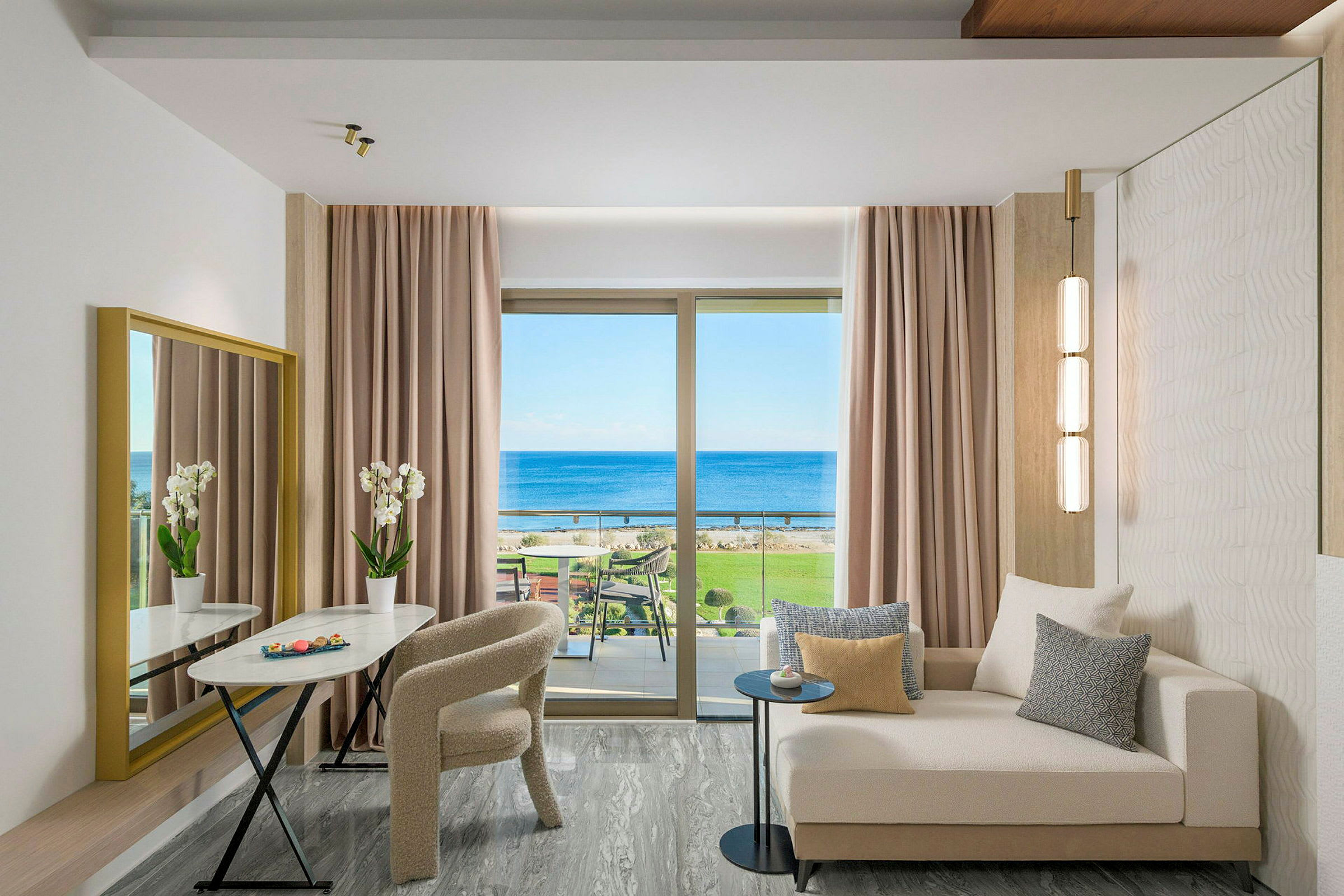 En moderne hotellsvit med soffa, bord, stolar och utsikt över havet genom ett stort fönster. (AI-genererad text)