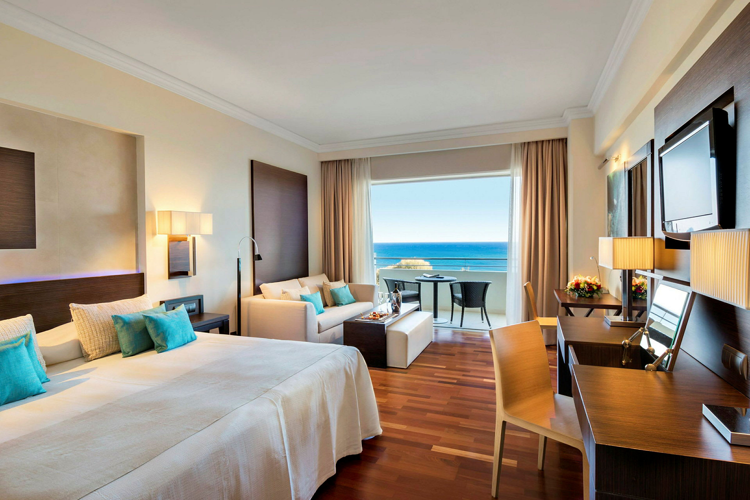 Hotellrum med dubbelsäng, sittgrupp och utsikt mot havet. (AI-genererad text)