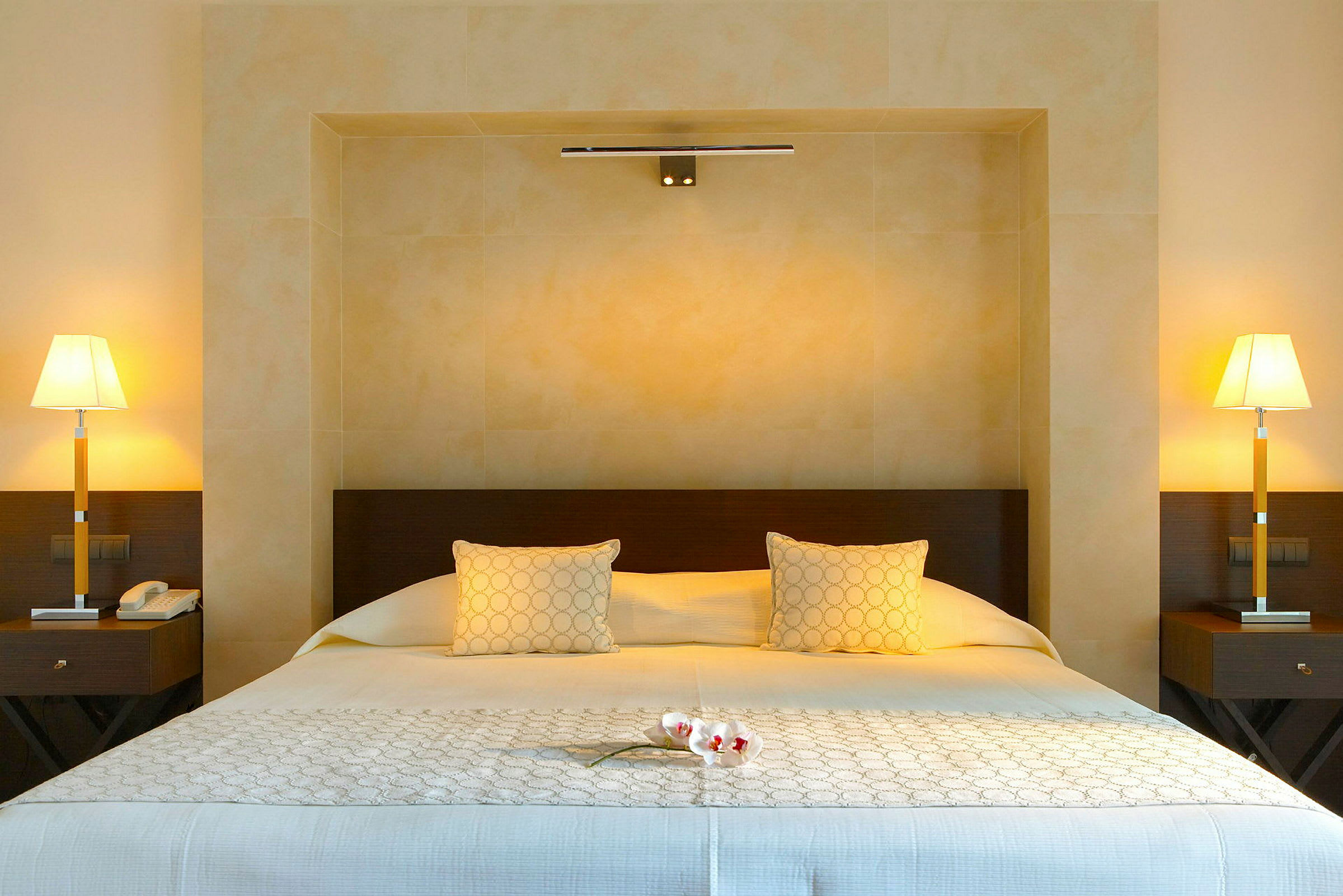 Hotellsäng med två sänglampor och blommor på täcket. (AI-genererad text)