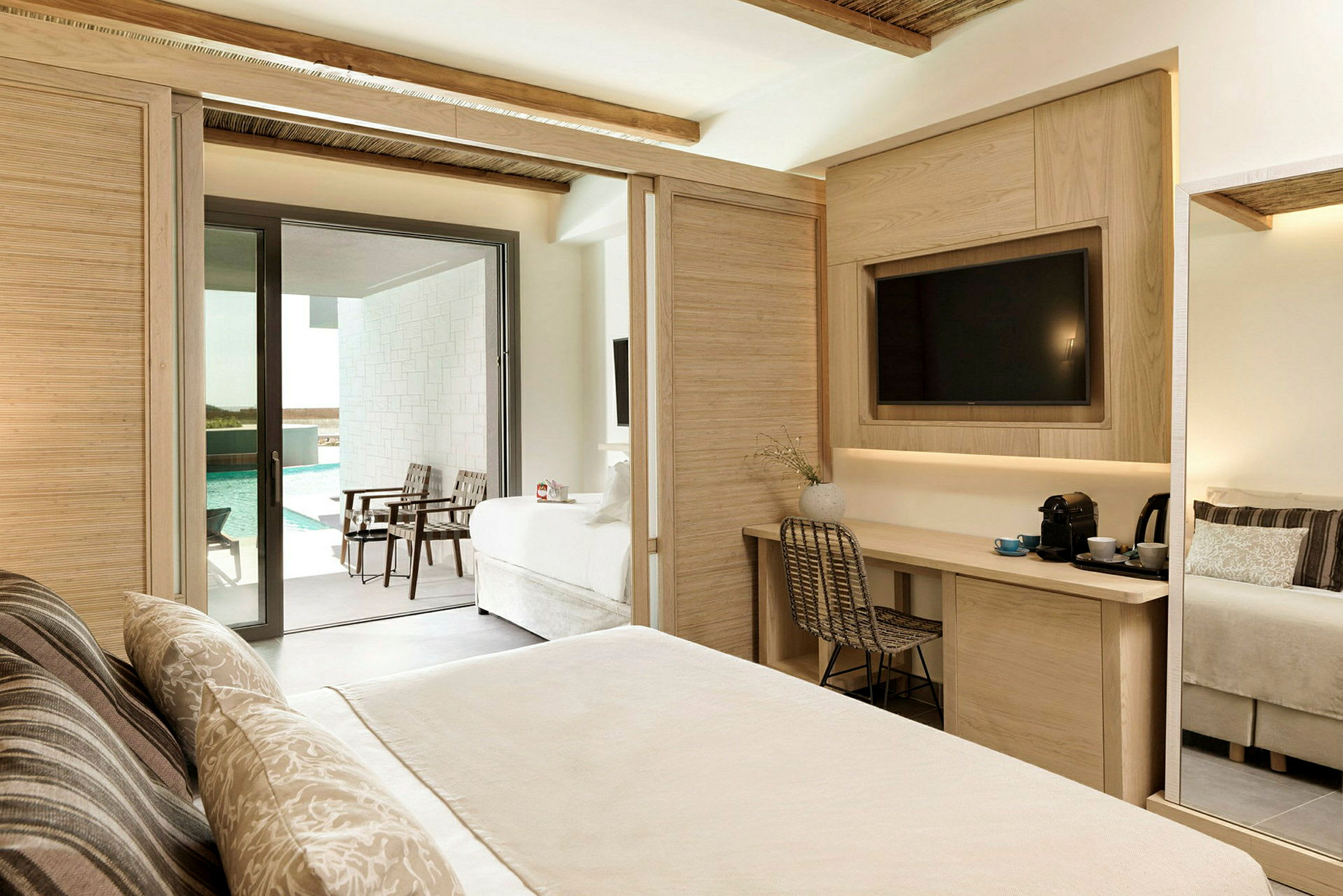 Ett hotellrum med en ljus inredning, en säng, ett skrivbord med stol, och en balkong som vetter mot en pool. (AI-genererad text)