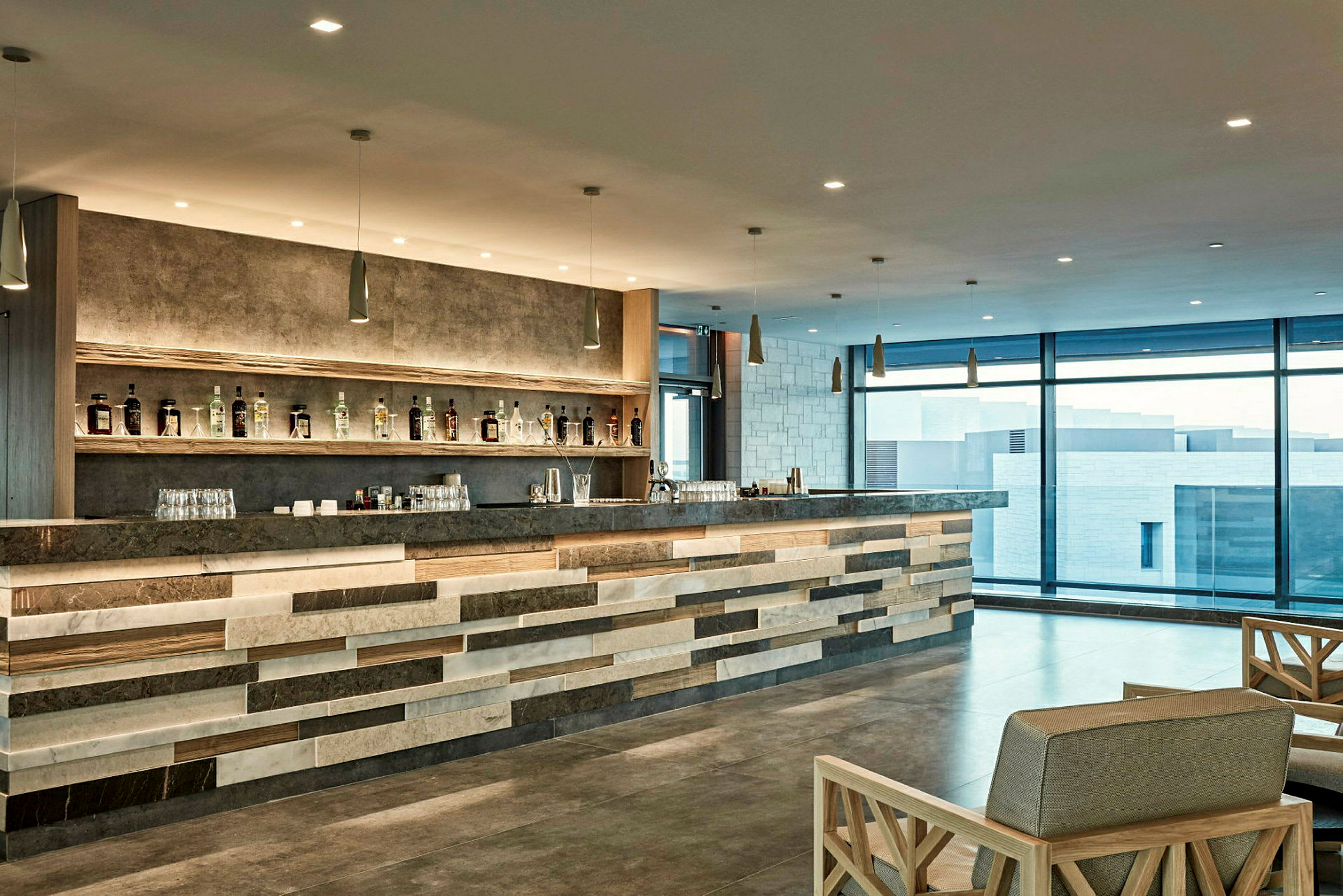 Modern bar med flaskor på hyllor och stolar framför. (AI-genererad text)