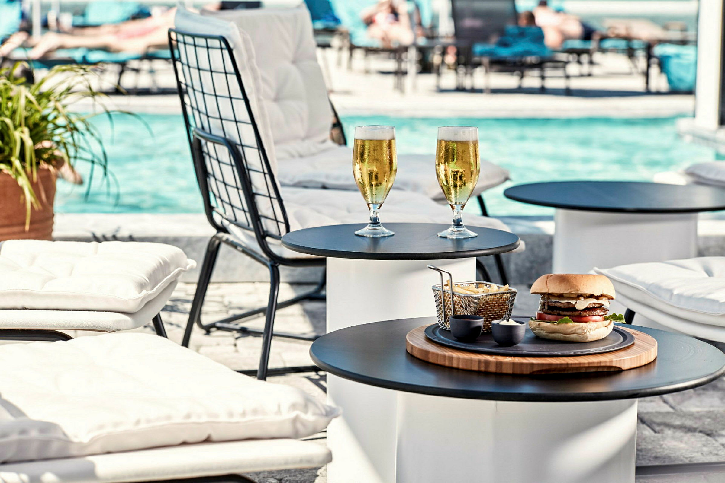 Solstolar vid en pool med dryck och hamburgare på ett bord. (AI-genererad text)