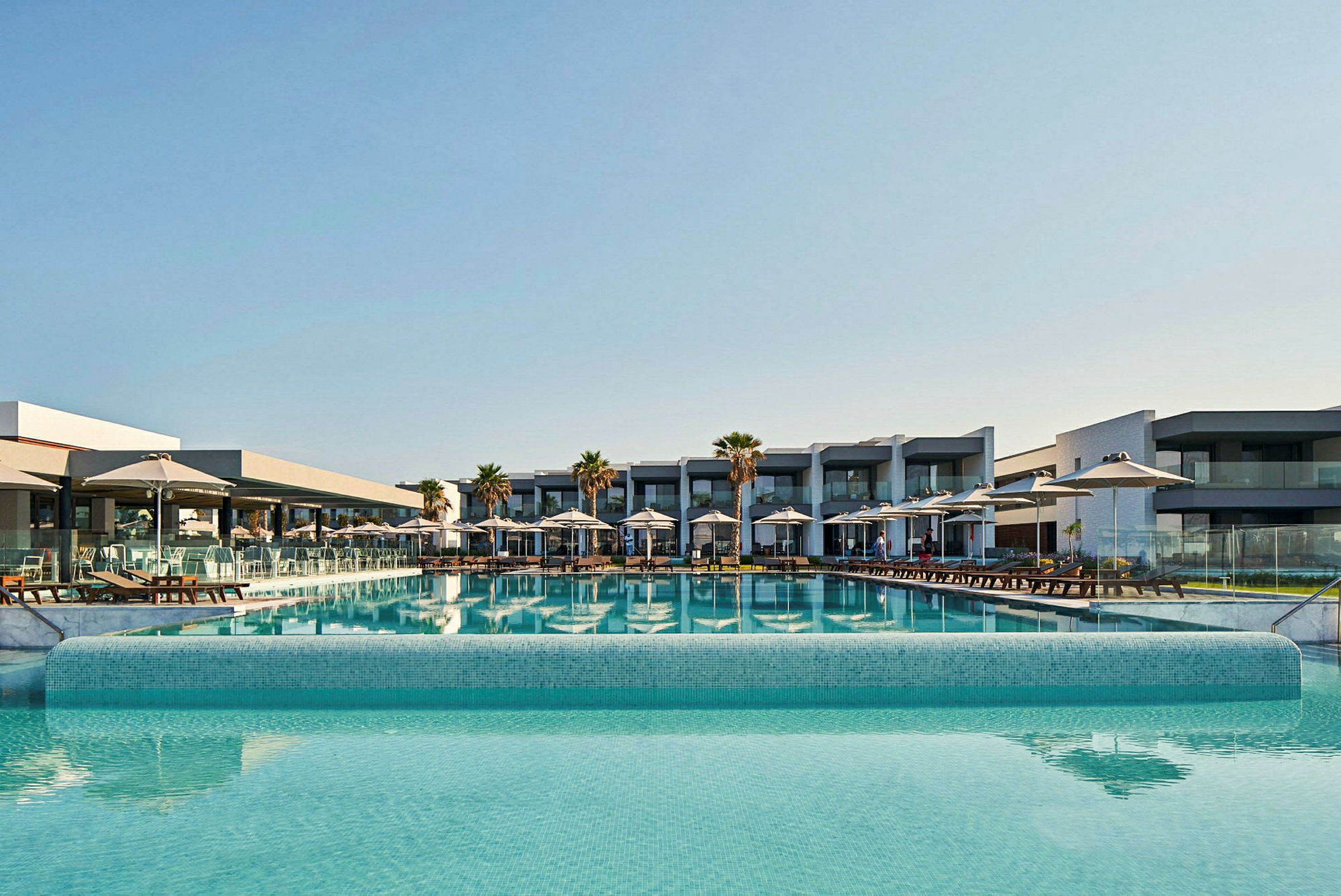 Modern hotellbyggnad med stor pool och solstolar. (AI-genererad text)
