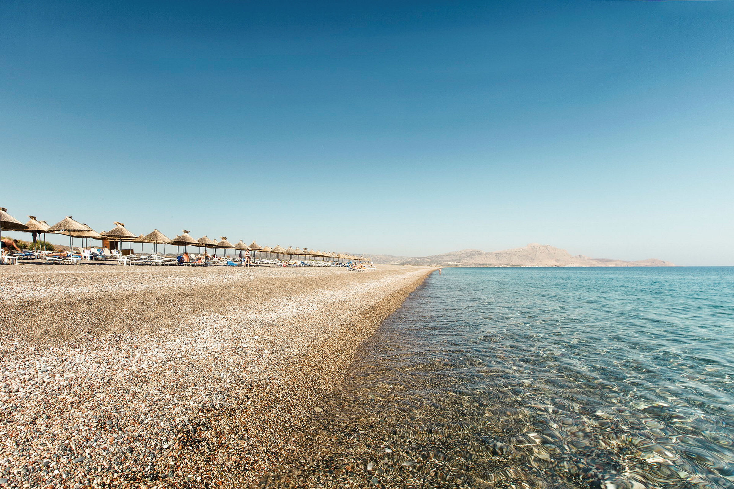 Vy över en strand med parasoller, solstolar och klart havsvatten. (AI-genererad text)