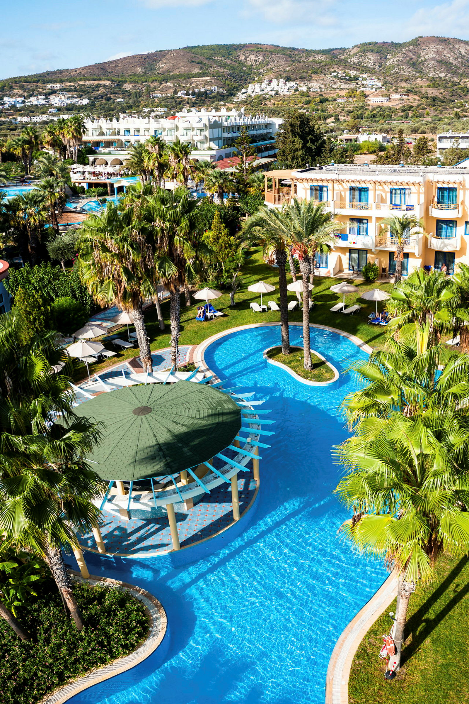 Hotellområde med pooler, palmer och byggnader i bakgrunden. (AI-genererad text)