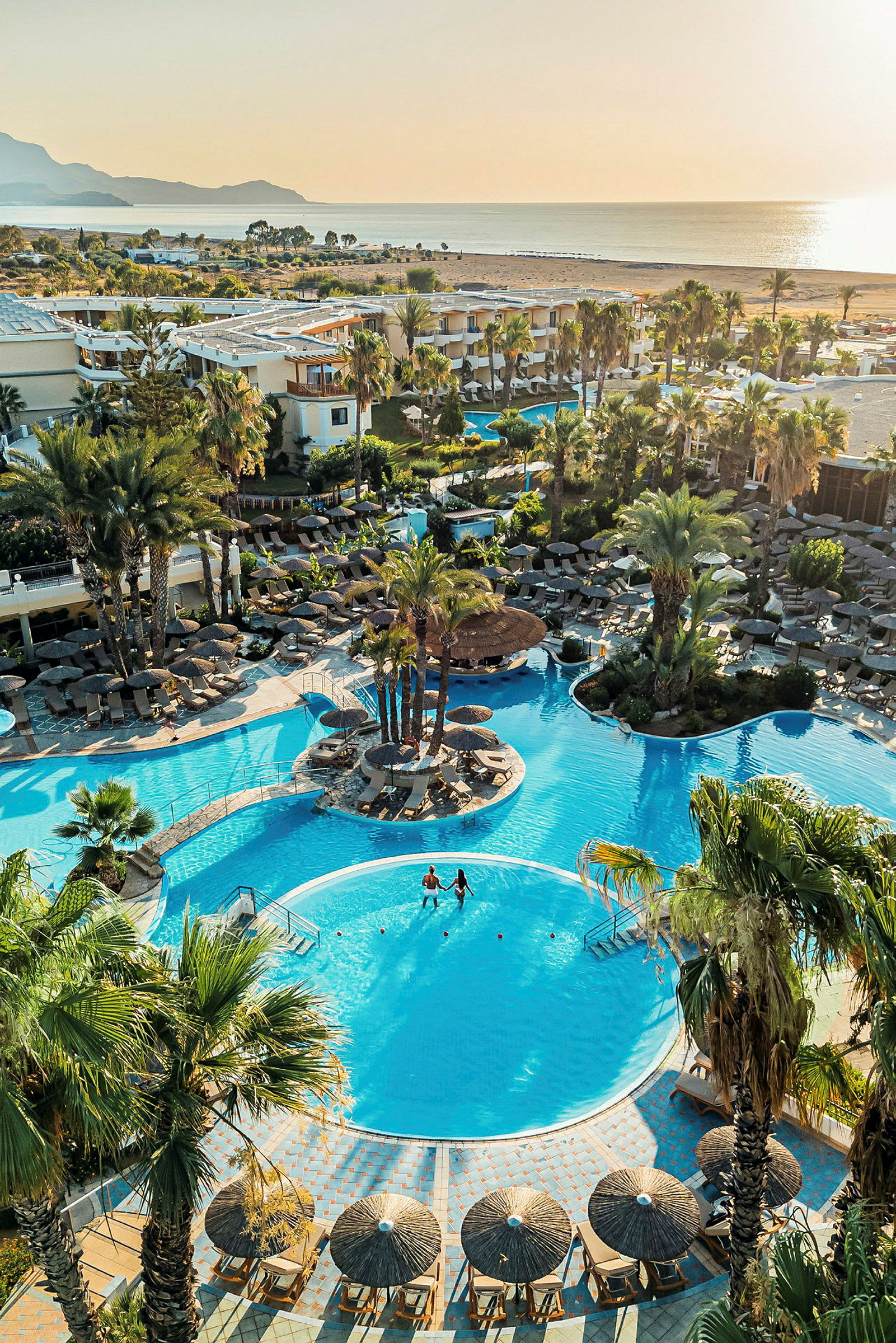 Hotellområde med palmomgiven pool och solstolar nära havet. (AI-genererad text)