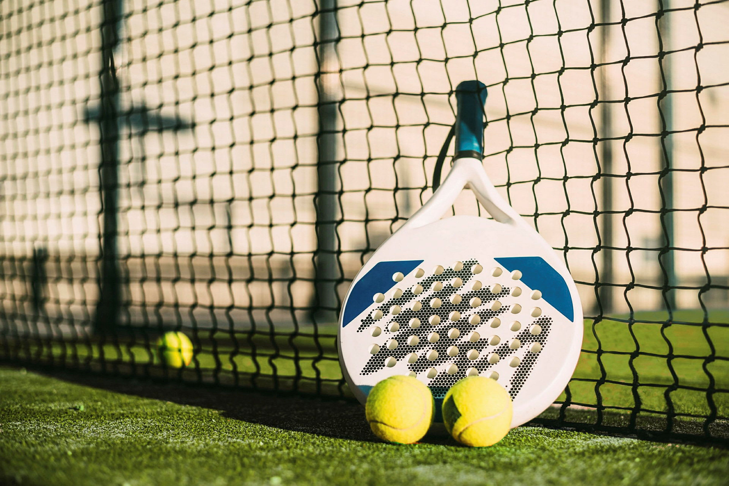 En padelracket och två bollar vid nätet på en padelbana. (AI-genererad text)