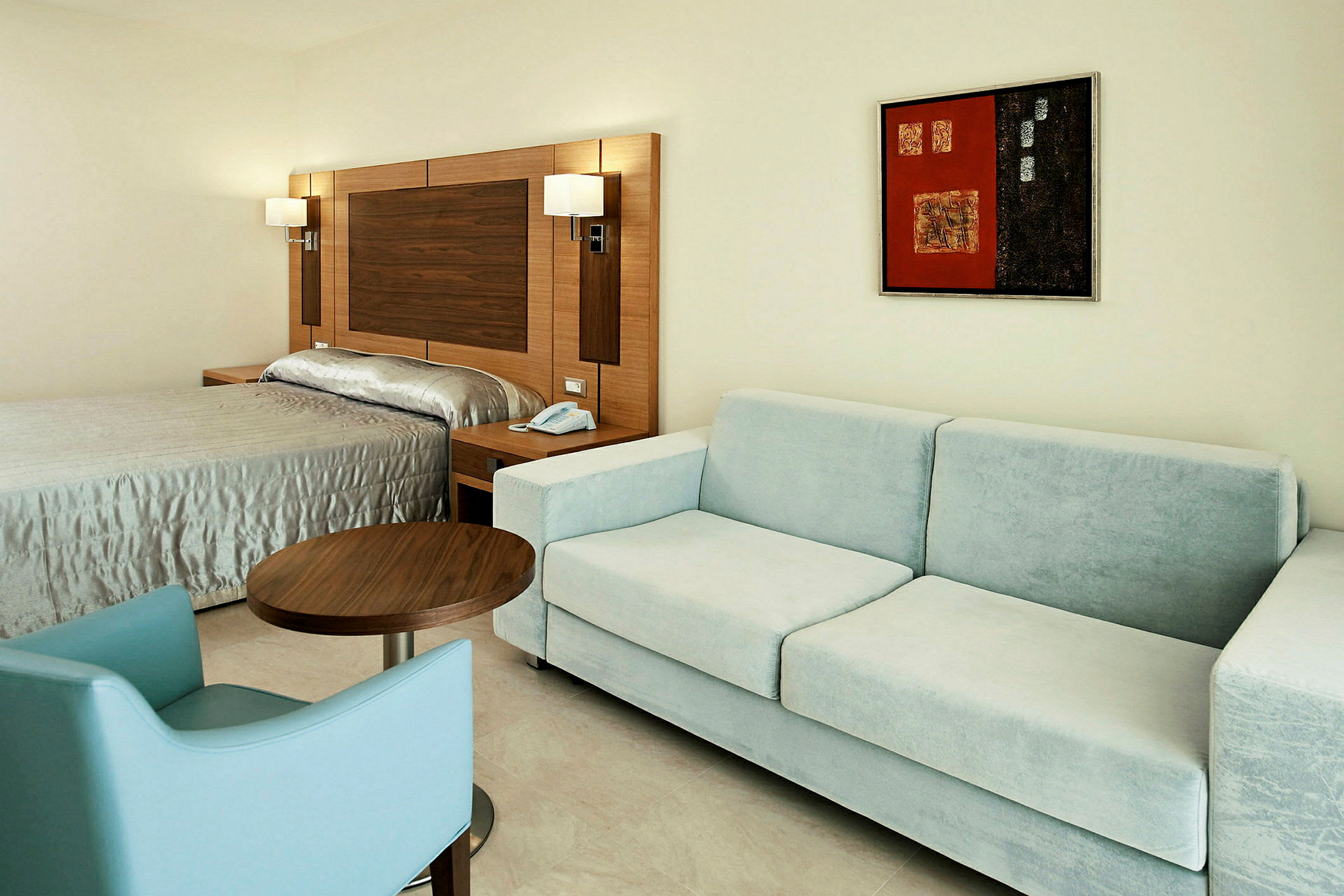 Ett hotellrum med en säng, en ljusblå soffa och ett bord. (AI-genererad text)
