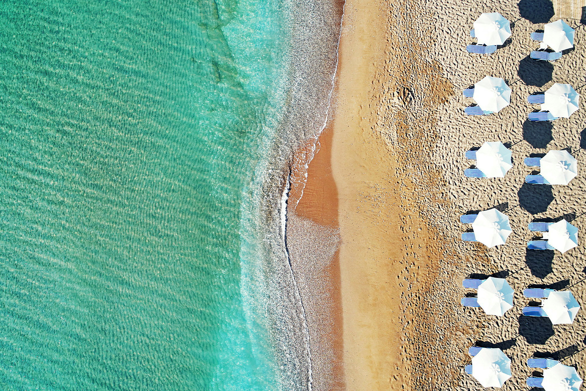 Flygfoto av en strand med parasoller och solstolar bredvid klart vatten. (AI-genererad text)