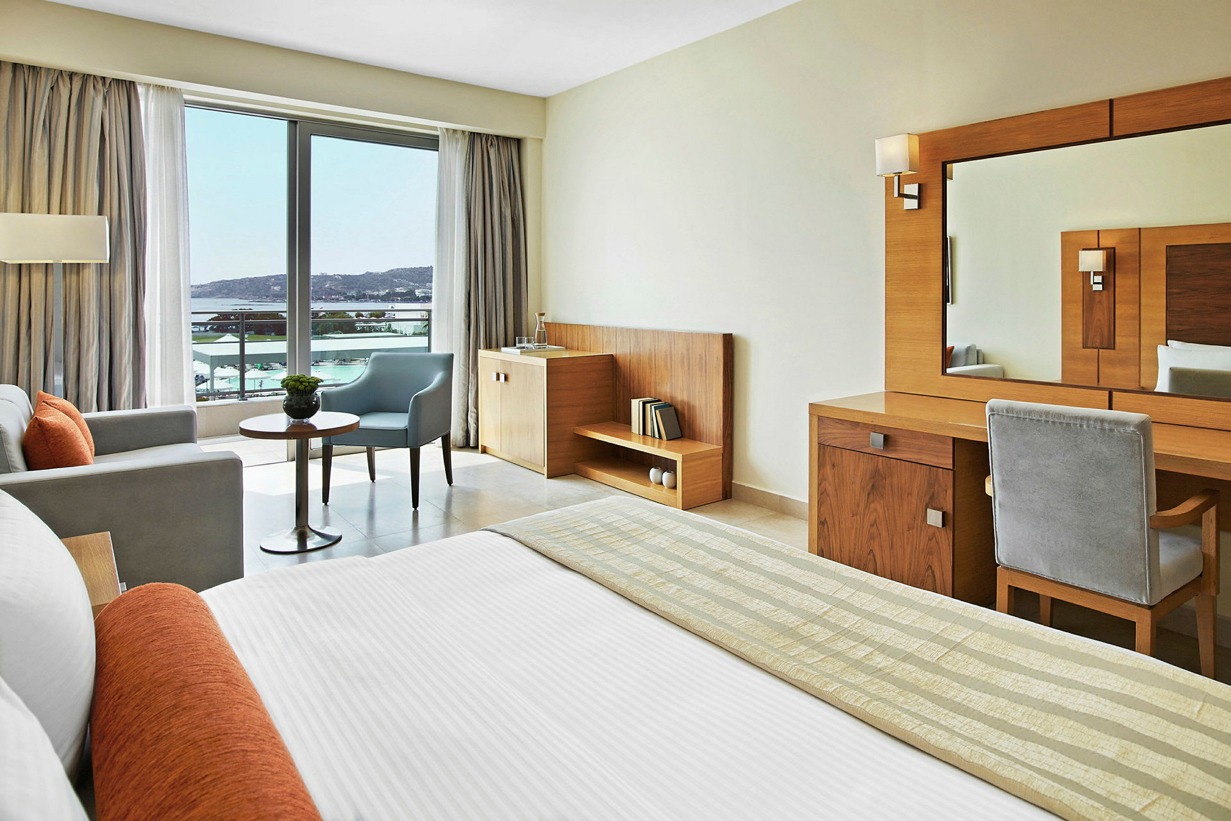 Hotellrum med modern inredning, säng, sittgrupp och utsikt över ett vattendrag genom en stor glasdörr. (AI-genererad text)
