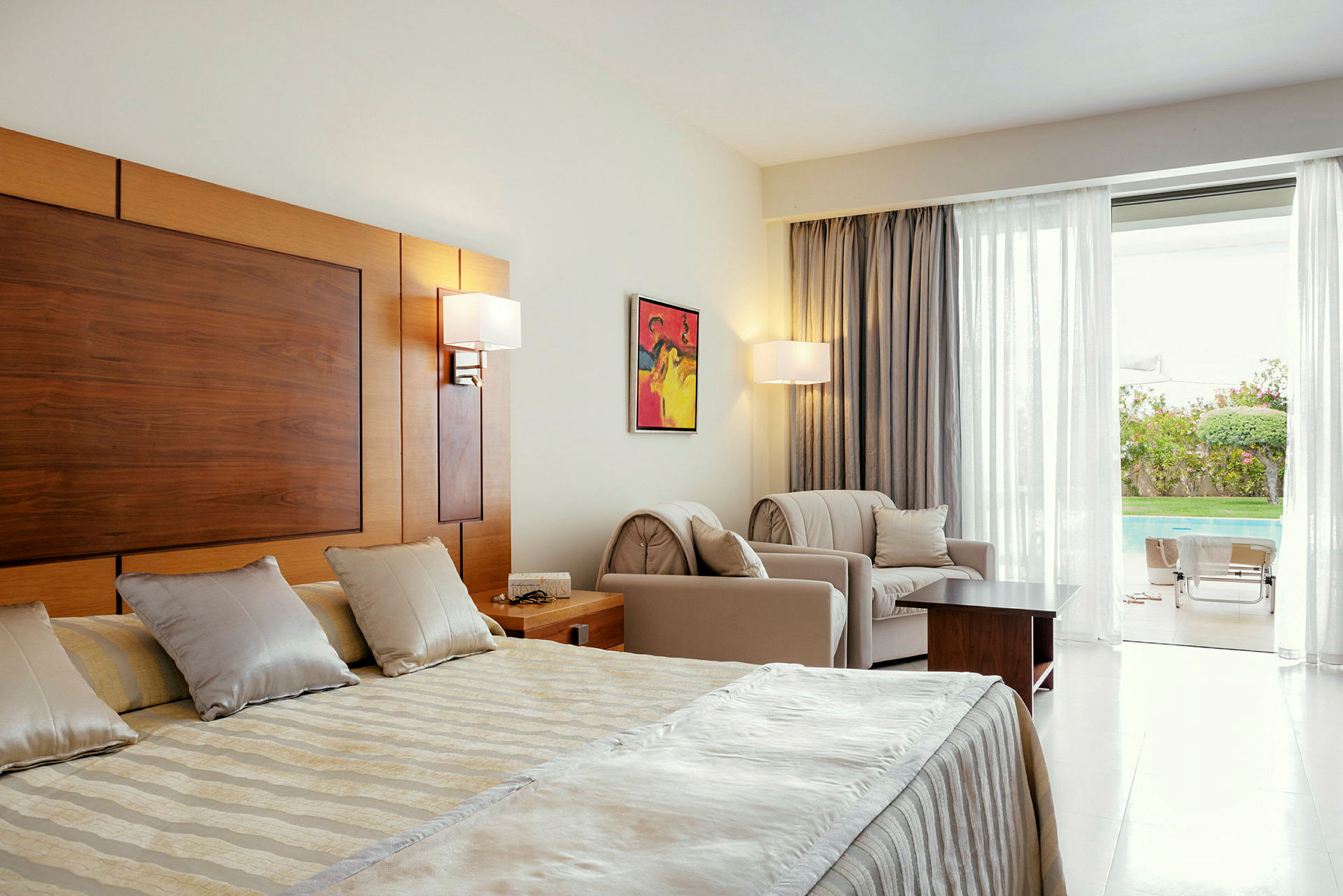 Ett hotellrum med en dubbelsäng, sittmöbler, och utsikt mot en pool utomhus. (AI-genererad text)