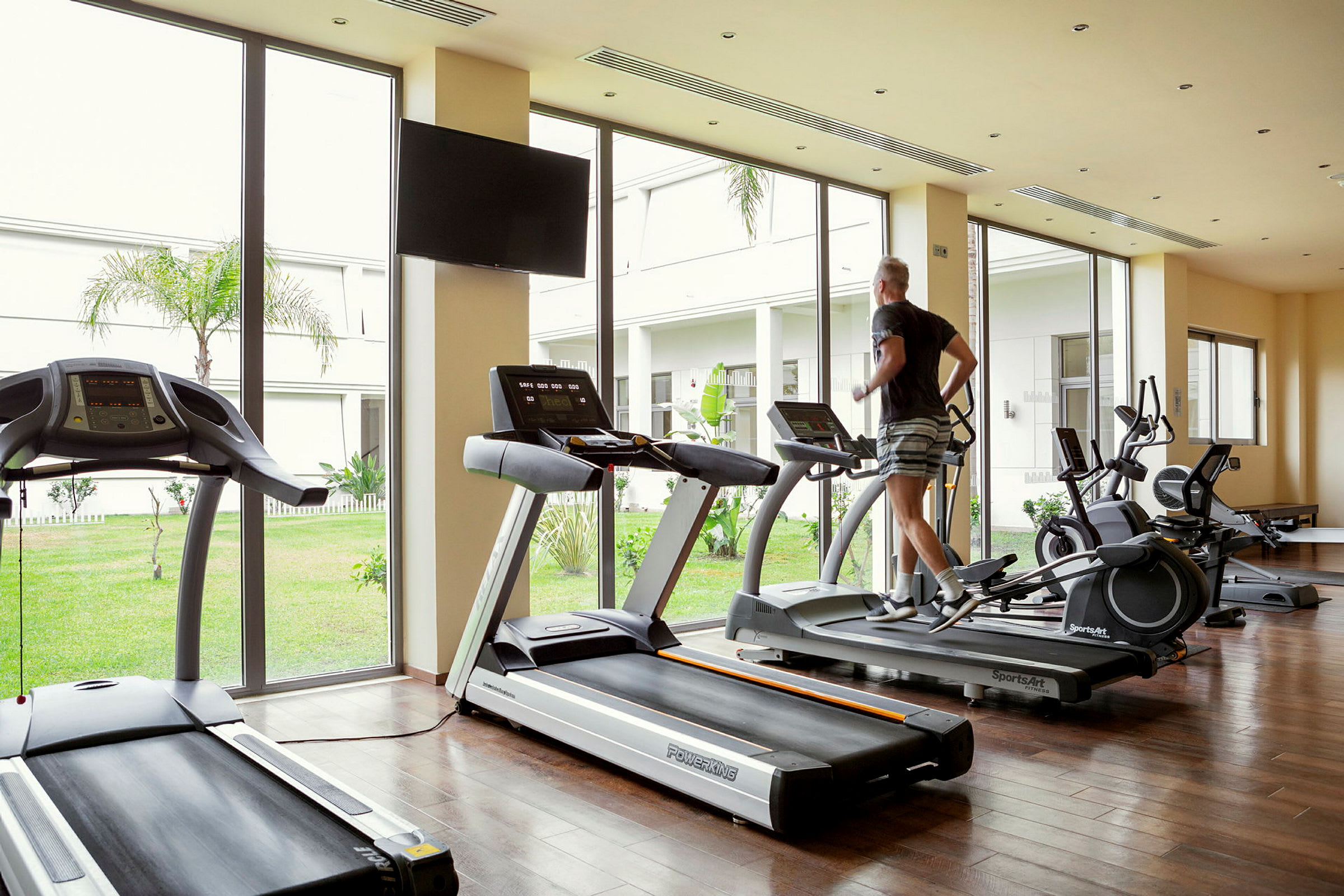 En person springer på ett löpband i ett gym med fönster mot en trädgård. (AI-genererad text)