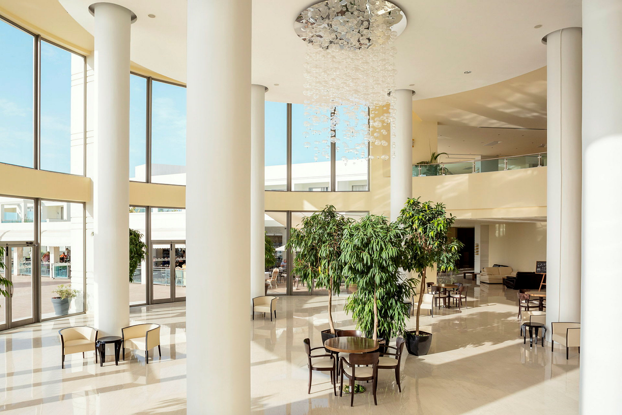 Ett hotellatrium med höga fönster, stolar och bord samt gröna växter. (AI-genererad text)