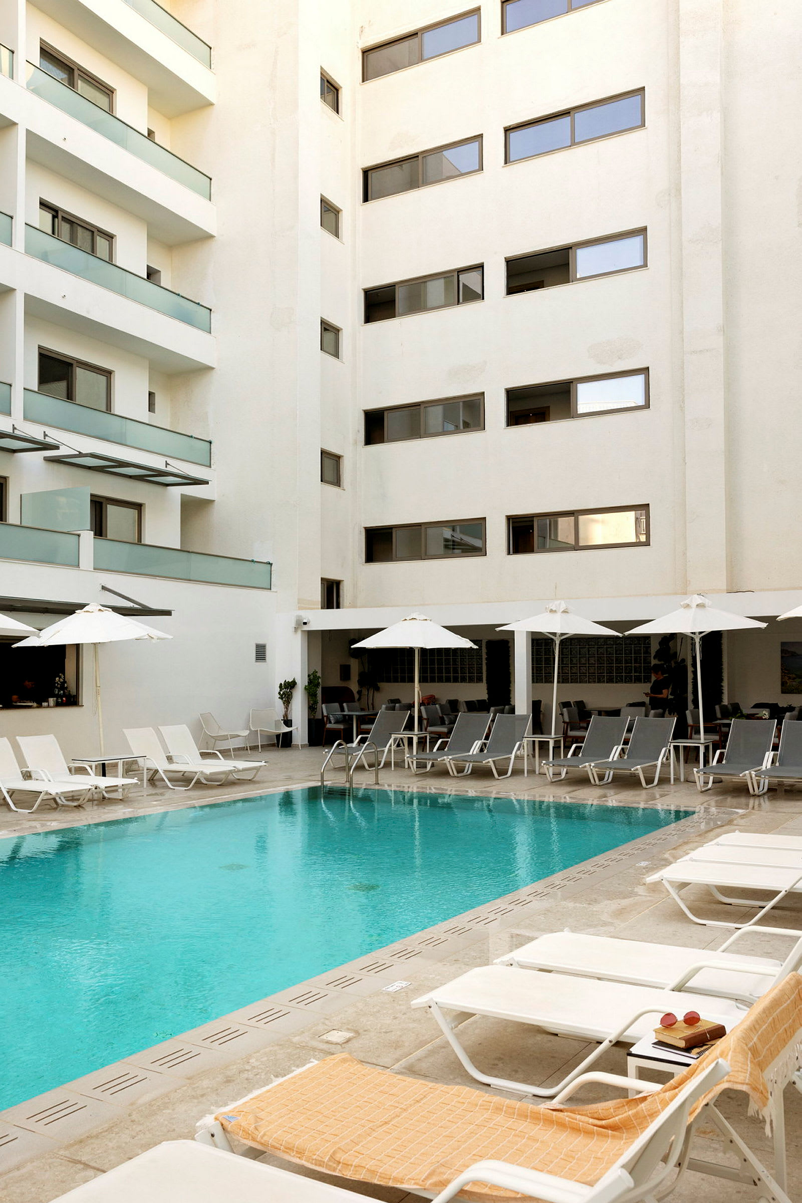 En pool vid ett flerbostadshus med solstolar och parasoller runtomkring. (AI-genererad text)