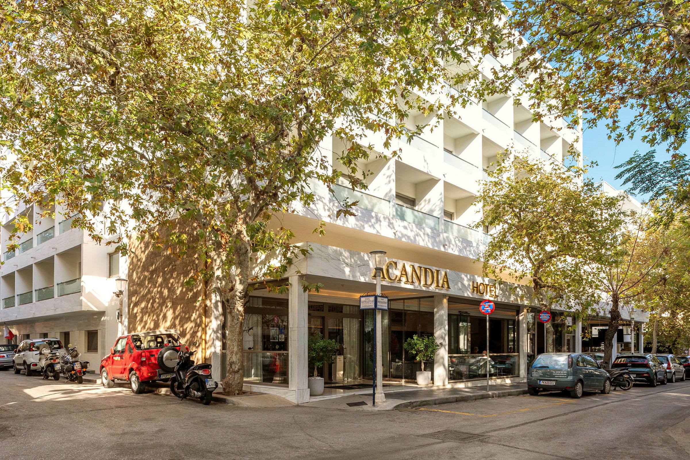 Hotellfasad med texten 'Candia Hotel', omgivna av träd och parkerade fordon. (AI-genererad text)