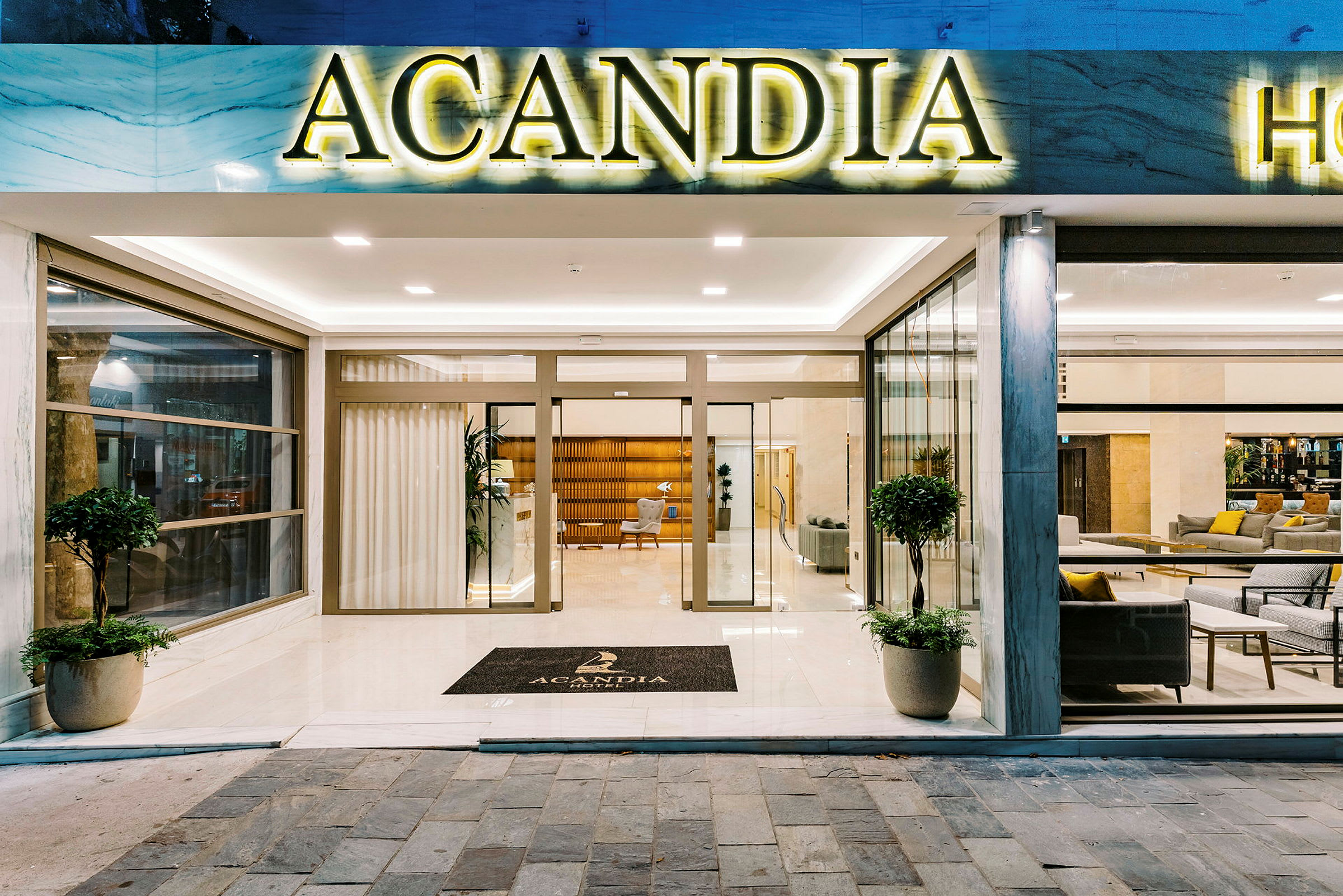 Ingången till Hotel Acandia med glasdörrar och en skylt med hotellets namn. (AI-genererad text)