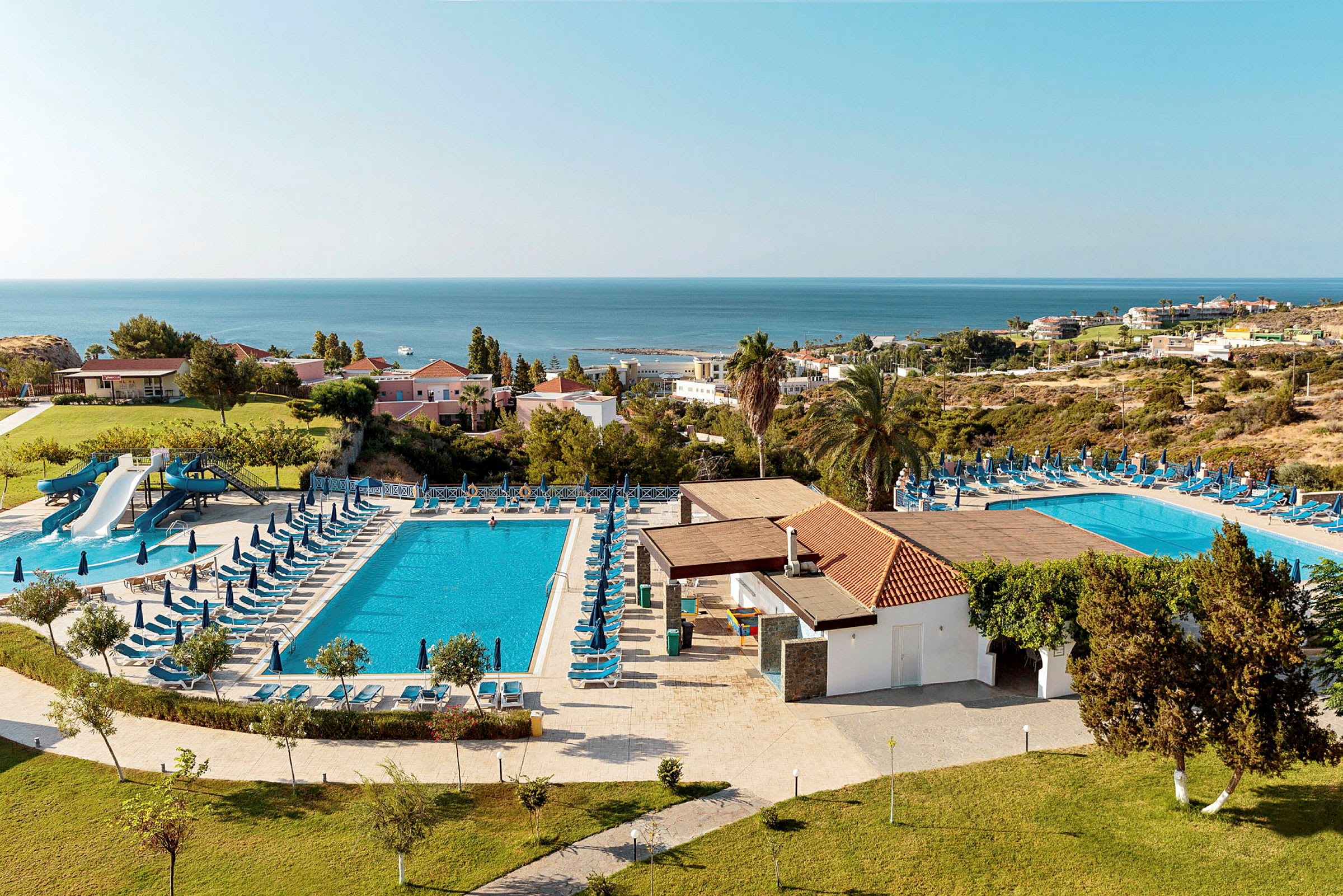 Vy över hotellområde med pooler, solstolar och havsutsikt. (AI-genererad text)