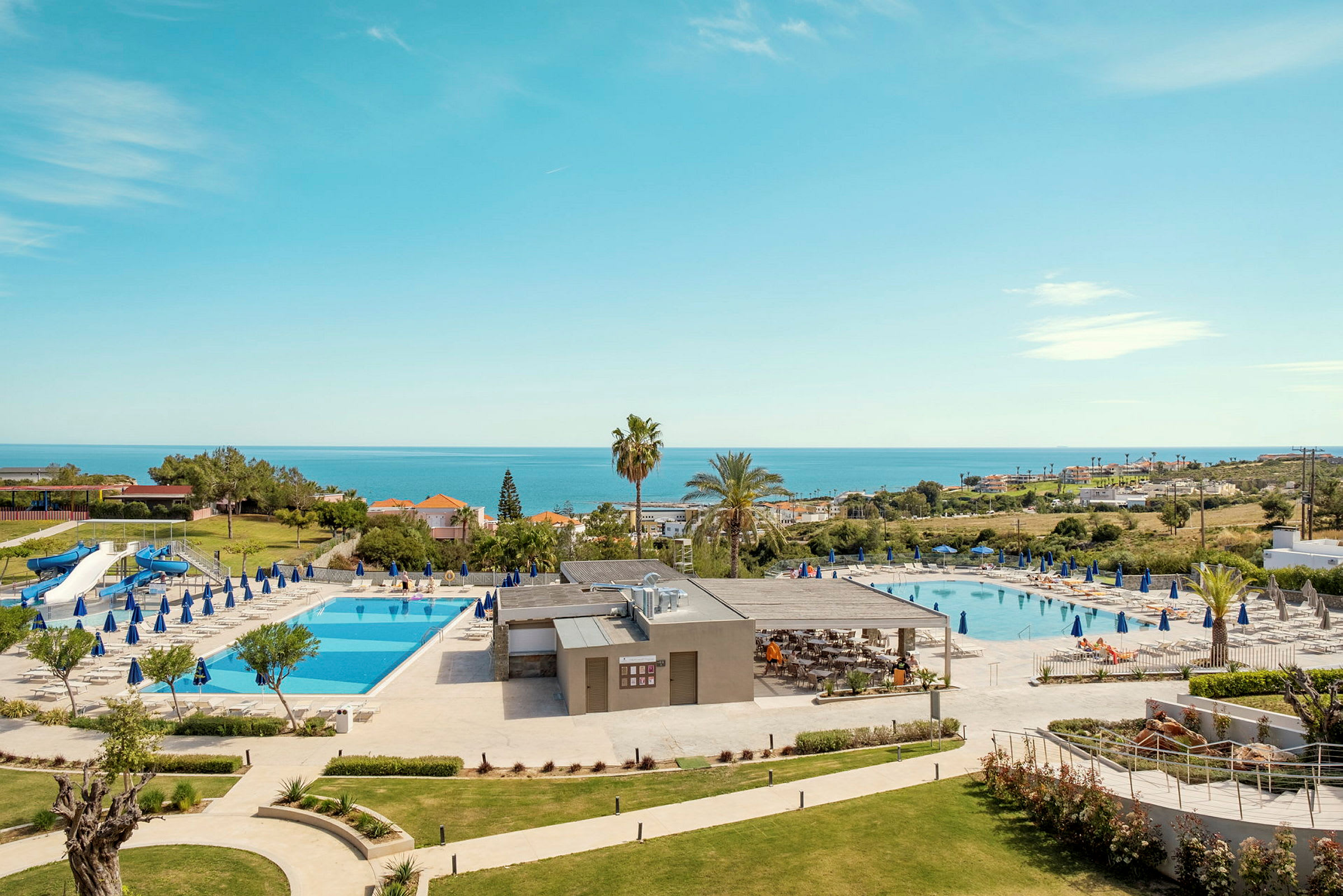 Hotellområde med två swimmingpooler, solstolar och havsutsikt. (AI-genererad text)