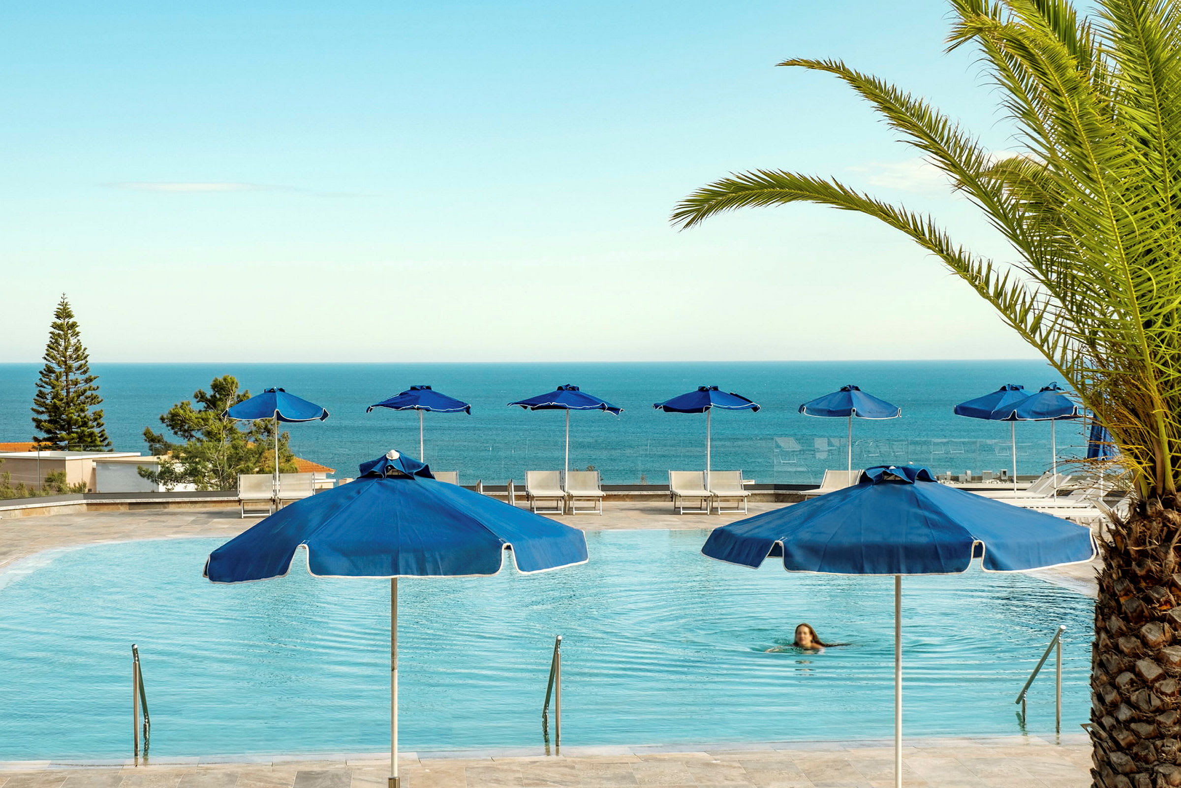 En pool med blå parasoller och utsikt över havet. (AI-genererad text)