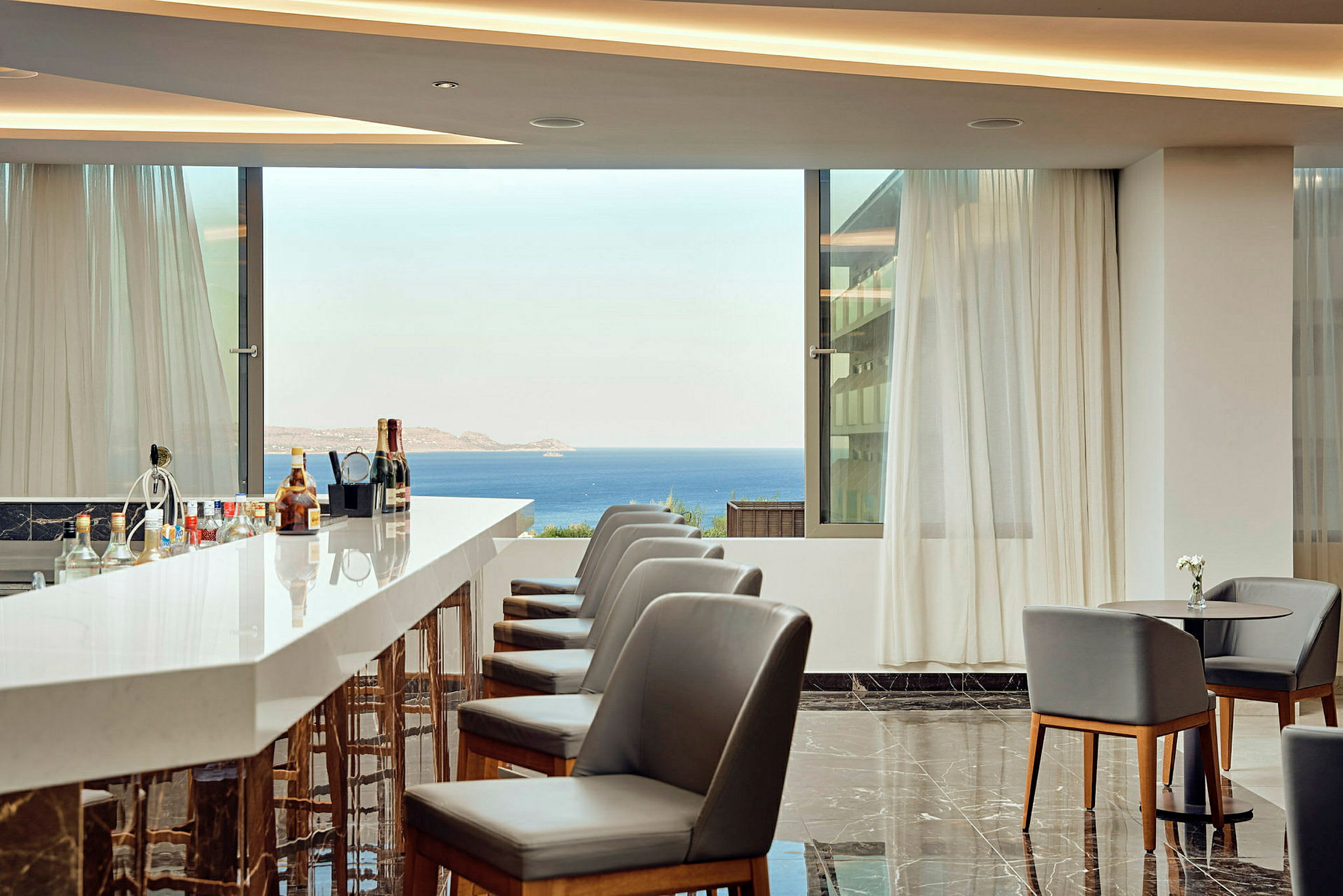 En hotellbar med moderna stolar, marmorgolv och utsikt över havet från stora fönster. (AI-genererad text)