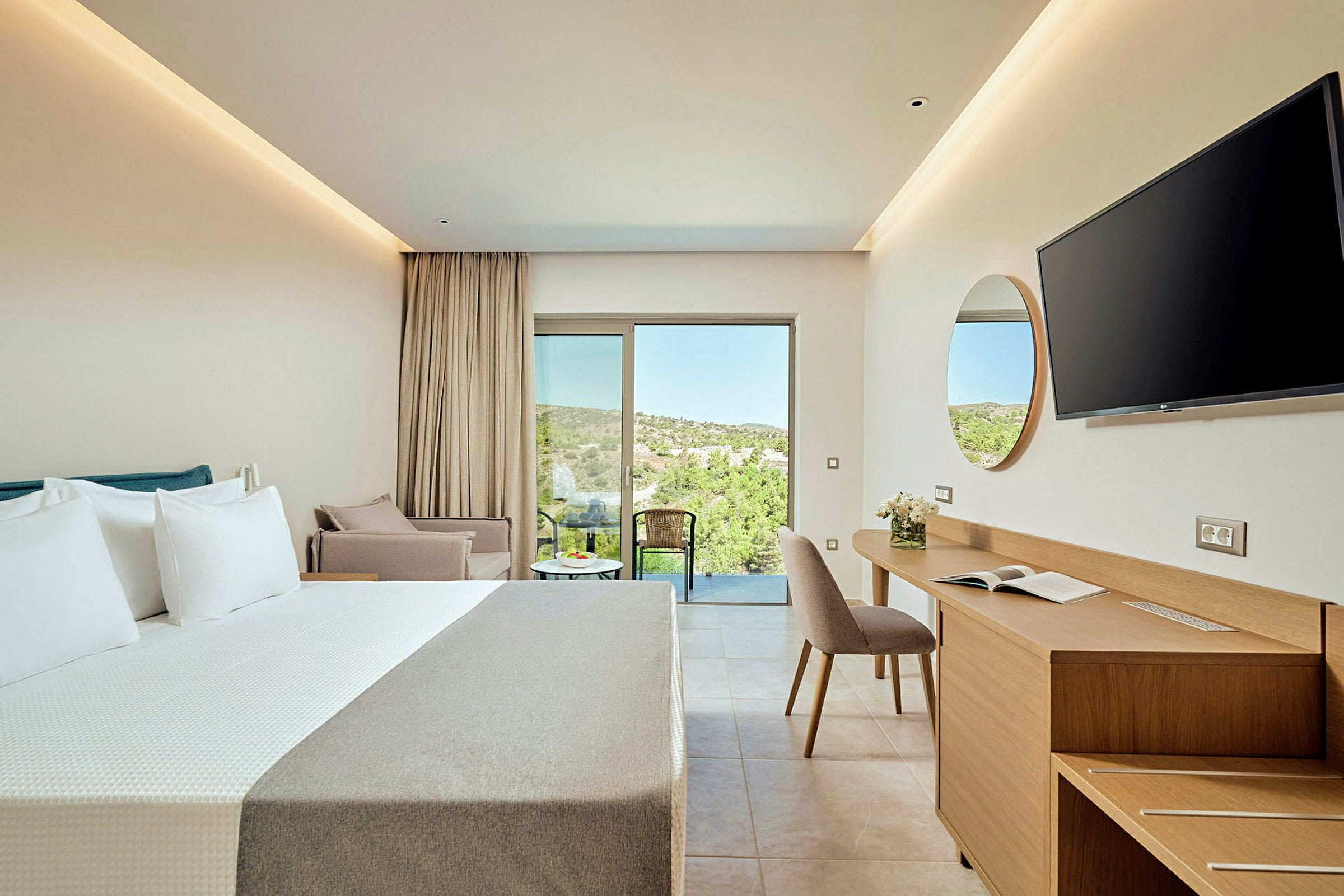 Ett modernt hotellrum med en dubbelsäng, skrivbord och stol samt en balkong med utsikt över grönskande terräng. (AI-genererad text)