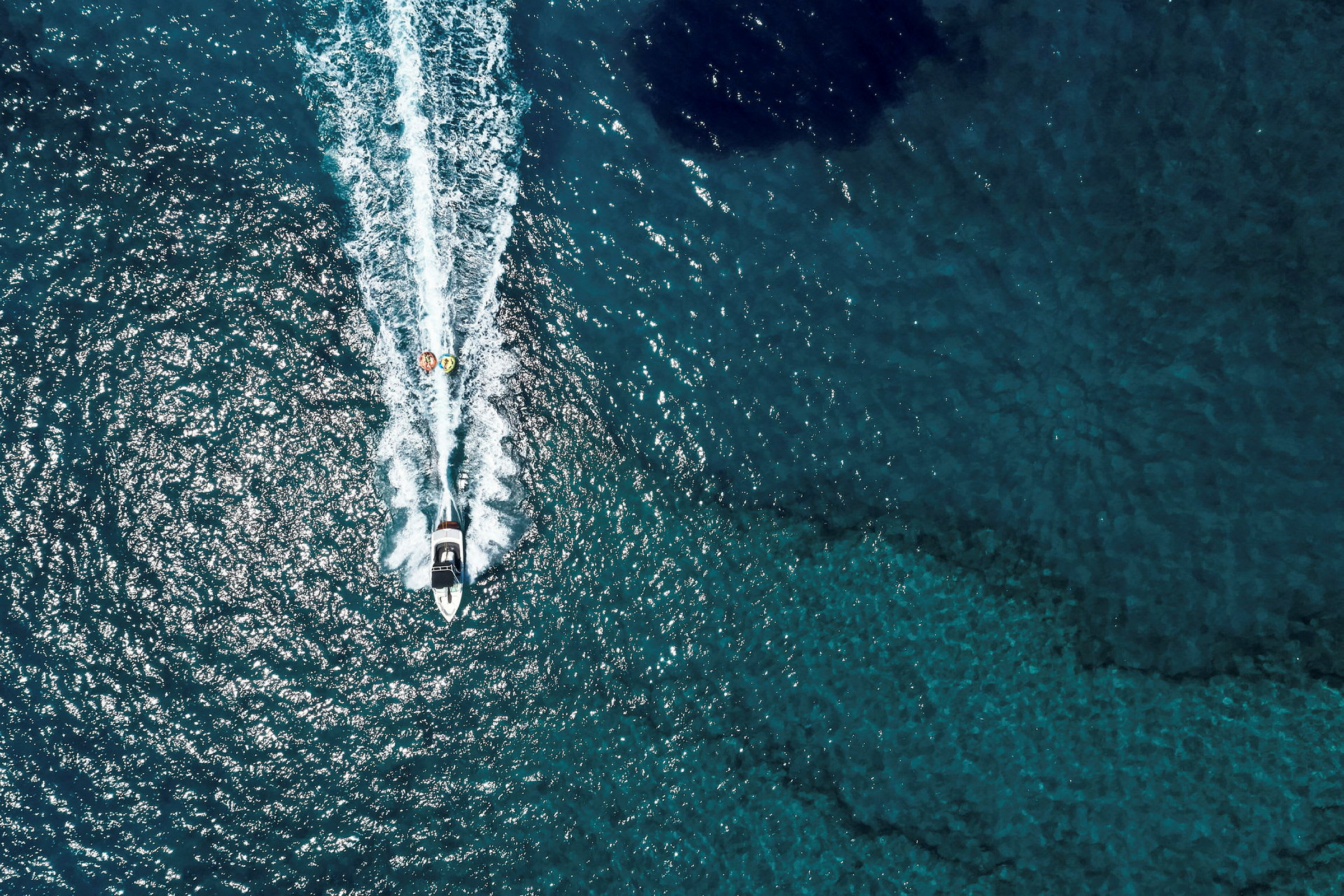 Flygbild av en motorbåt som drar två uppblåsbara flottar på havet. (AI-genererad text)