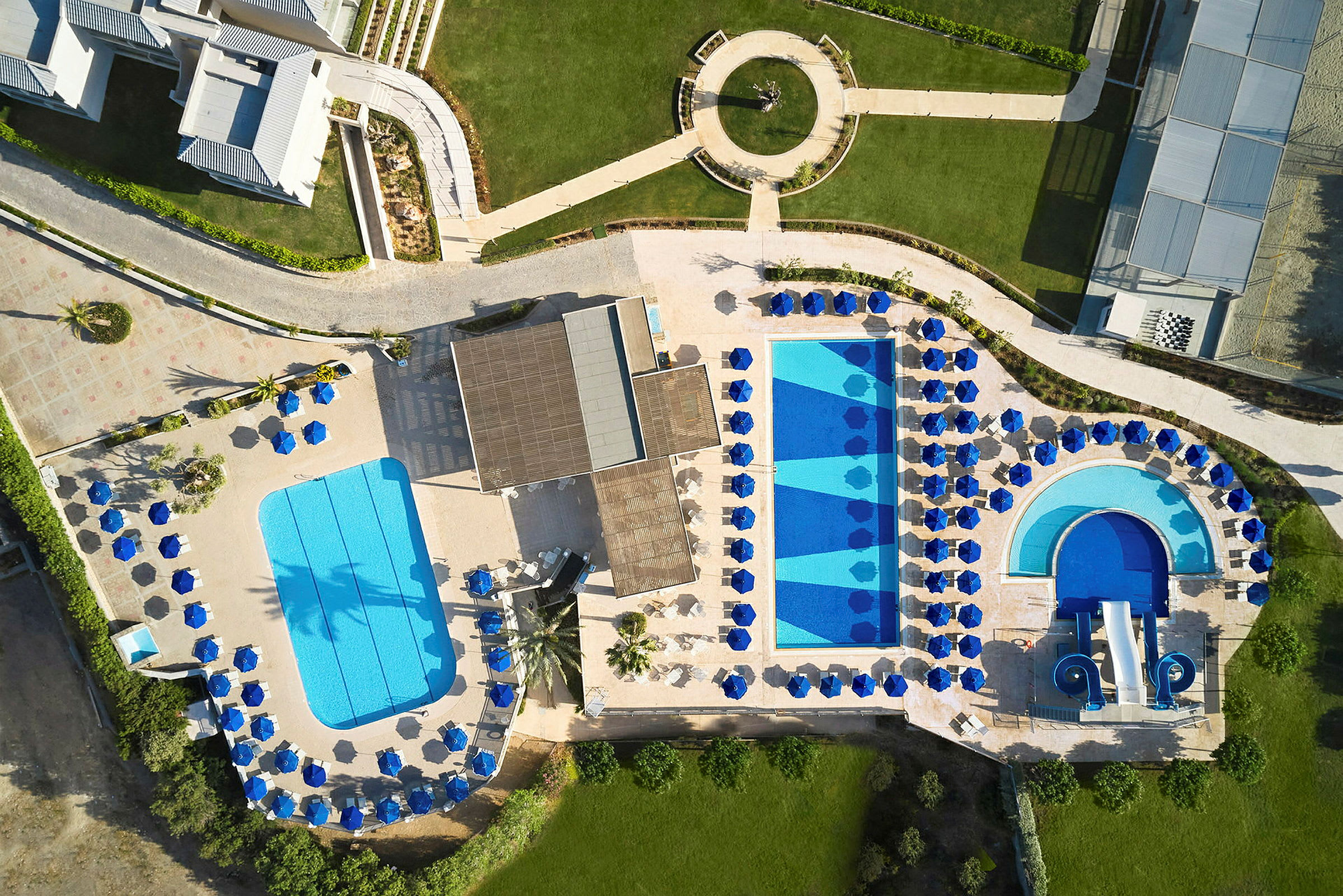Flygbild av en resort med pooler, solstolar och grönytor. (AI-genererad text)