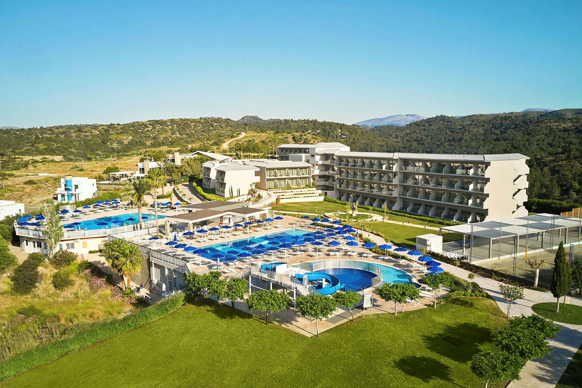 En vy över ett hotellområde med flera byggnader, pooler och solstolar, omgiven av grönska. (AI-genererad text)