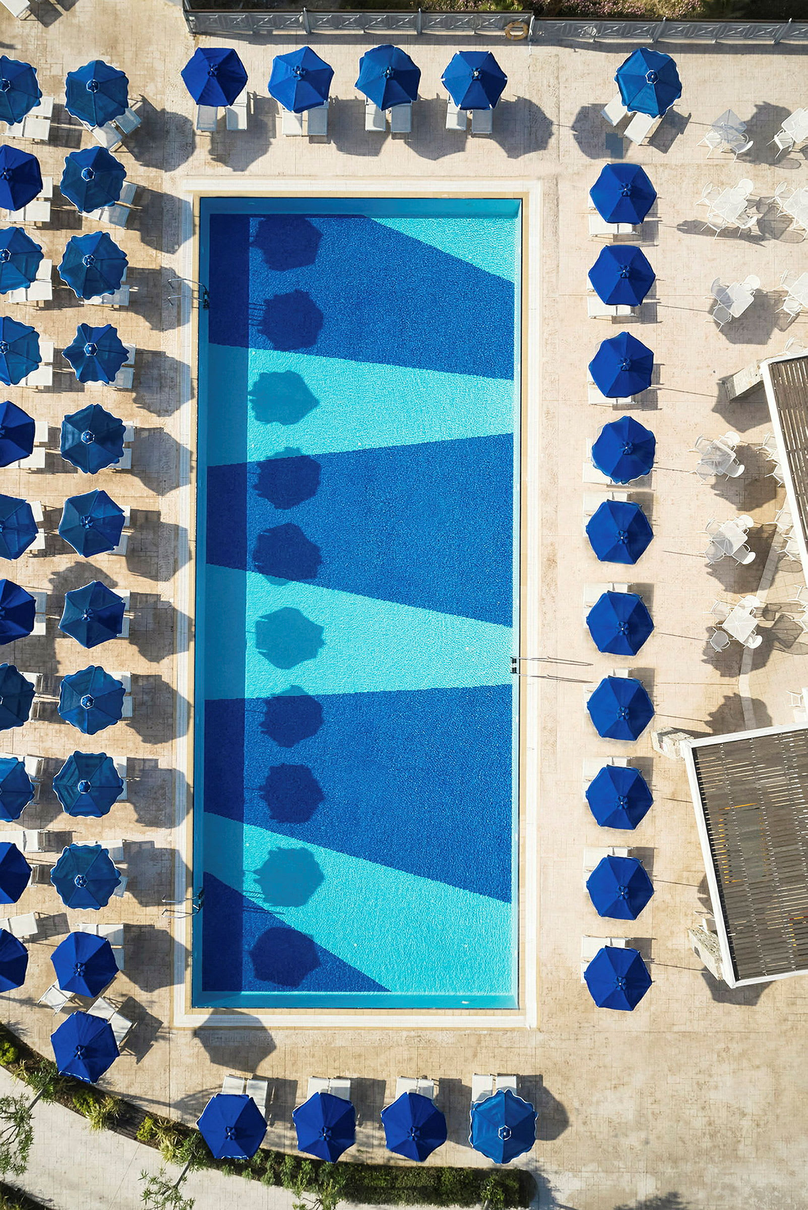 Fågelperspektiv av en swimmingpool omgiven av solstolar och parasoller. (AI-genererad text)