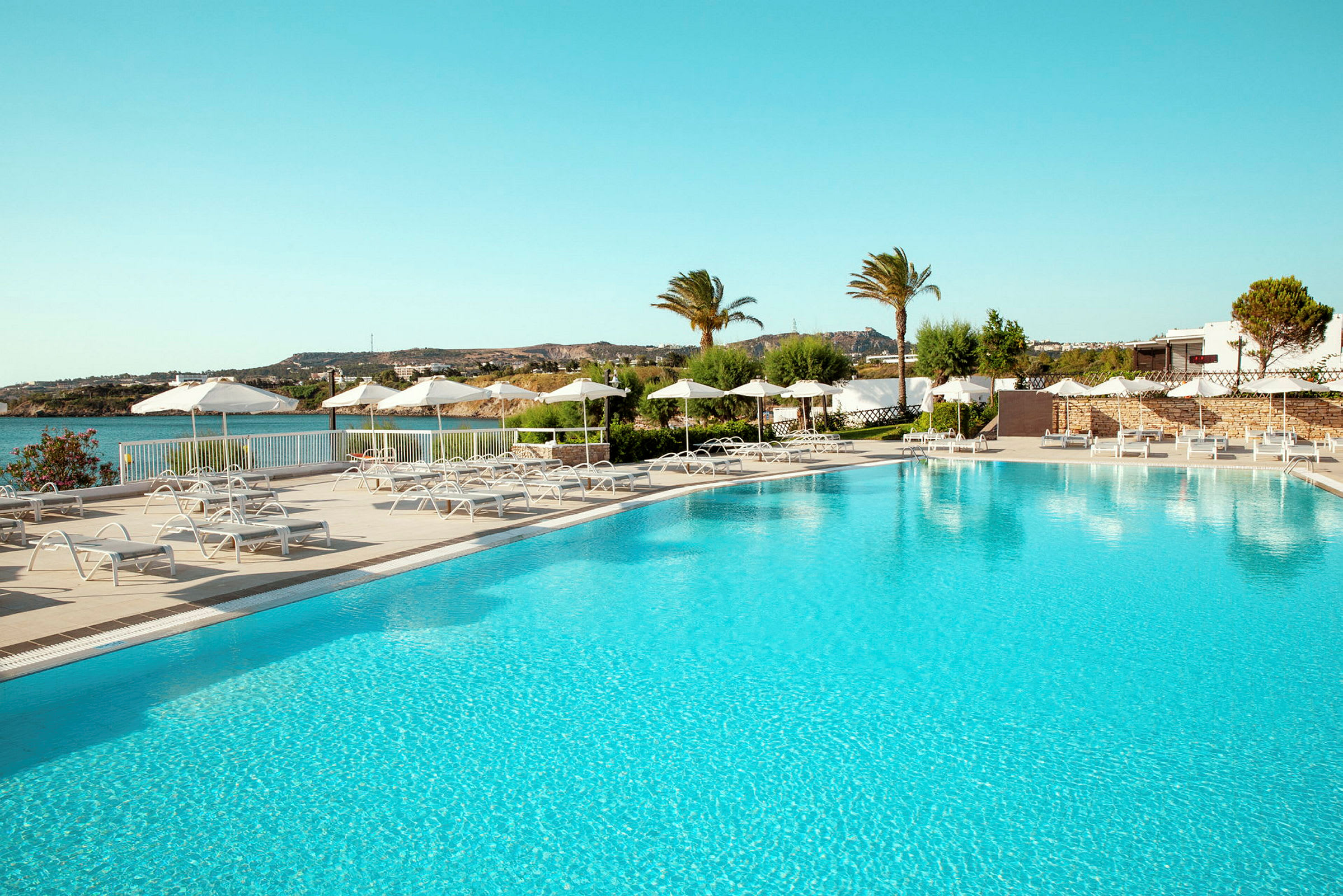 En pool med solstolar och parasoller vid en kust. (AI-genererad text)