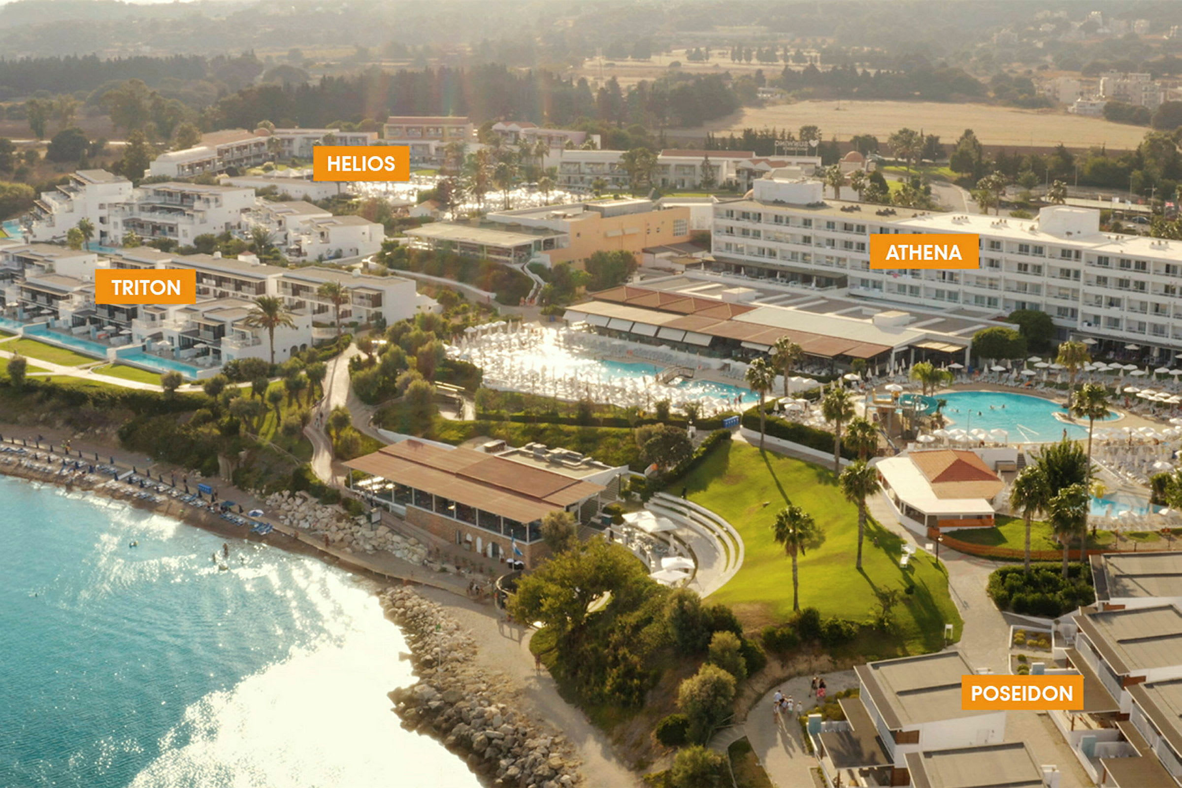 Flygbild av resort med flera hotellbyggnader och en pool nära en strand. (AI-genererad text)