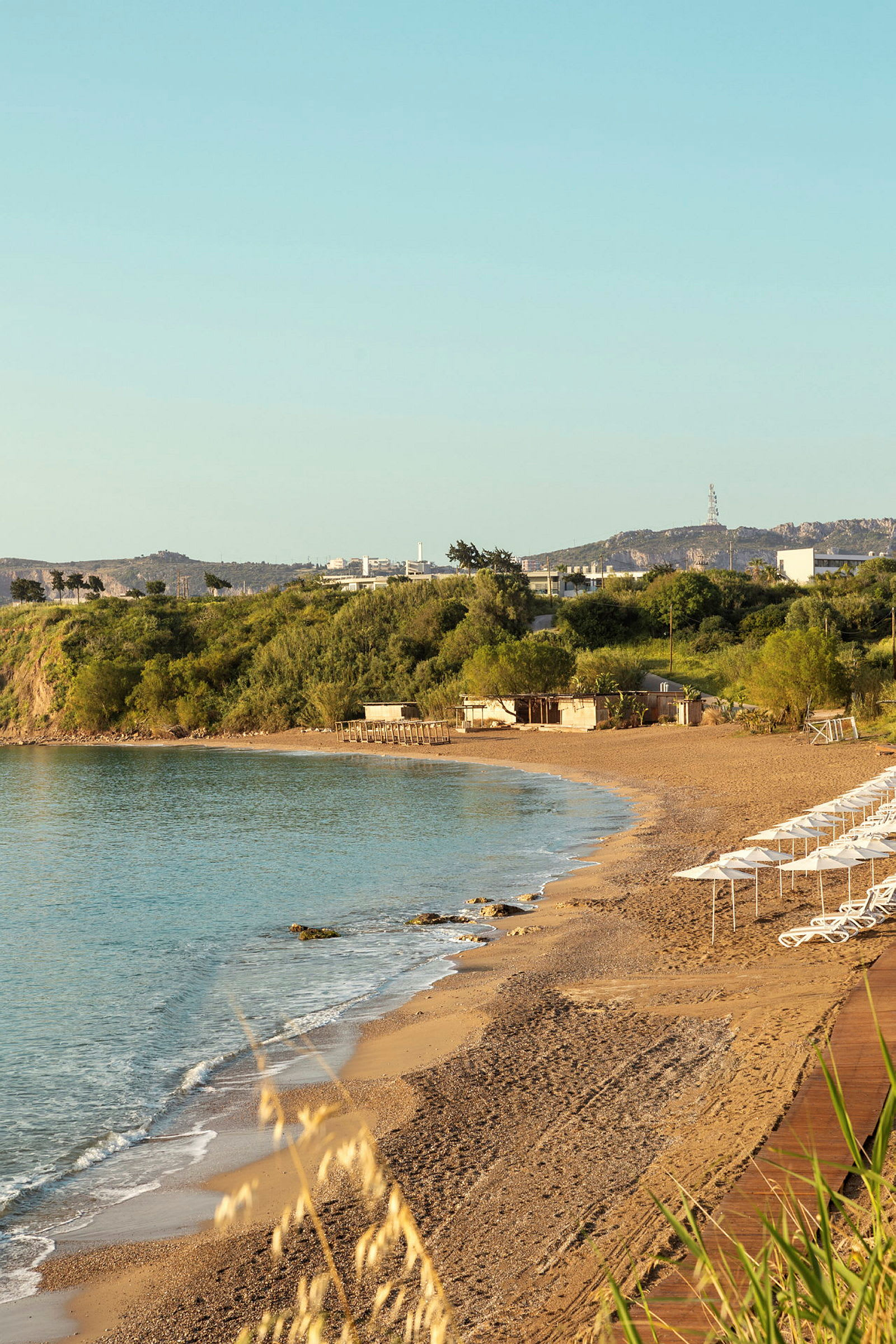 Strand med parasoller och solstolar vid havet, omgiven av grönska. (AI-genererad text)