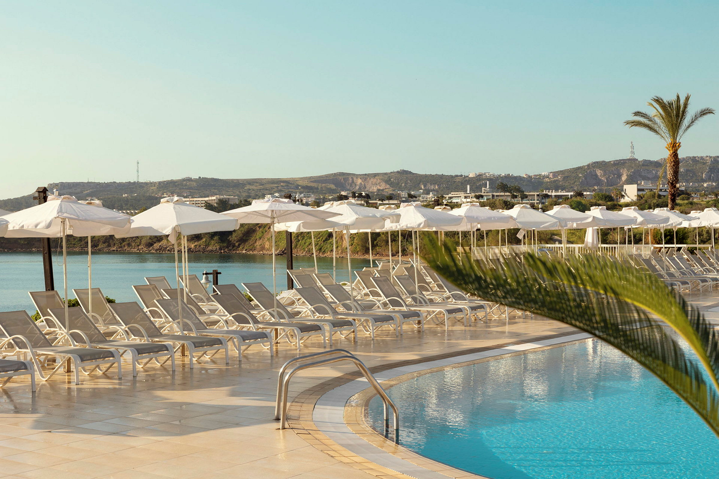 Solstolar och parasoller vid en pool med utsikt mot landskap och himmel. (AI-genererad text)