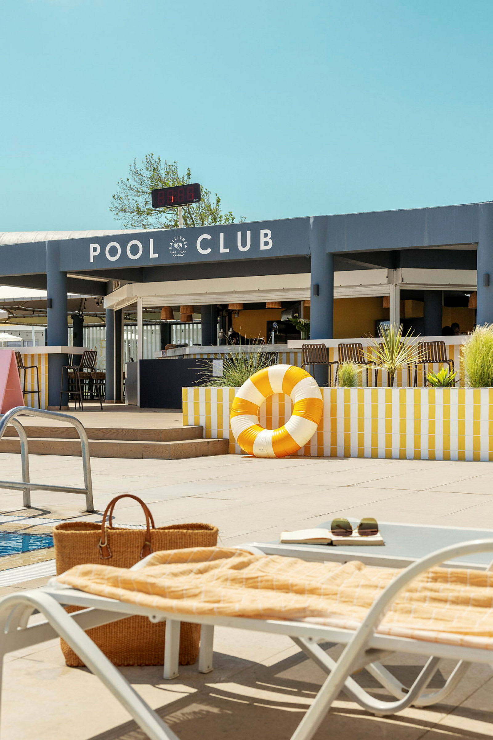 Utomhusområde vid en pool, med en vit och gul randig livboj och vilstolar. (AI-genererad text)
