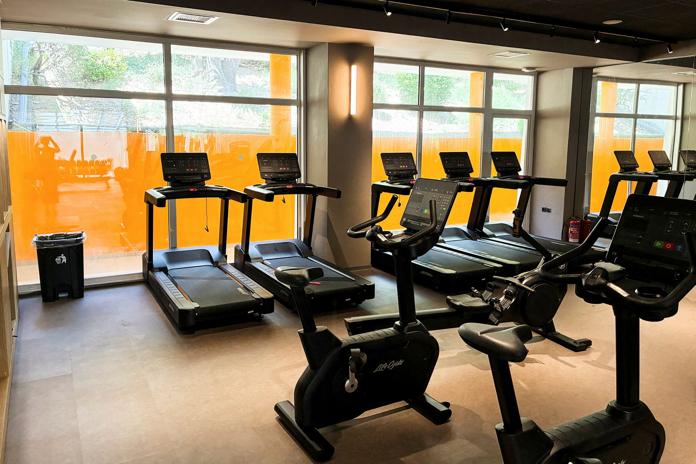 Ett gym med löpband och motionscyklar vid stora fönster. (AI-genererad text)