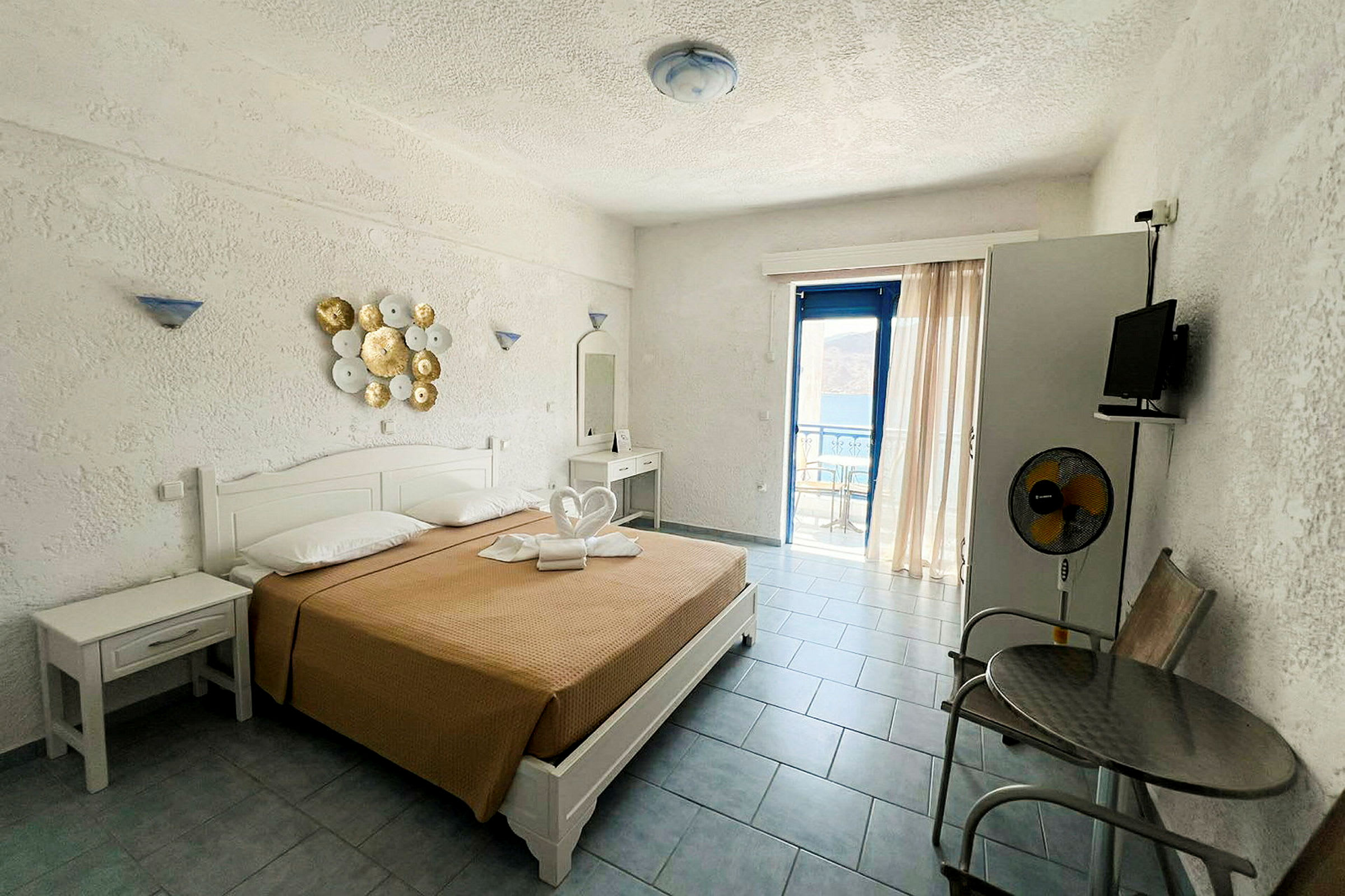 Ett hotellrum med en dubbelsäng, dekorerad med handdukar, och utsikt genom en glasdörr mot en balkong. (AI-genererad text)