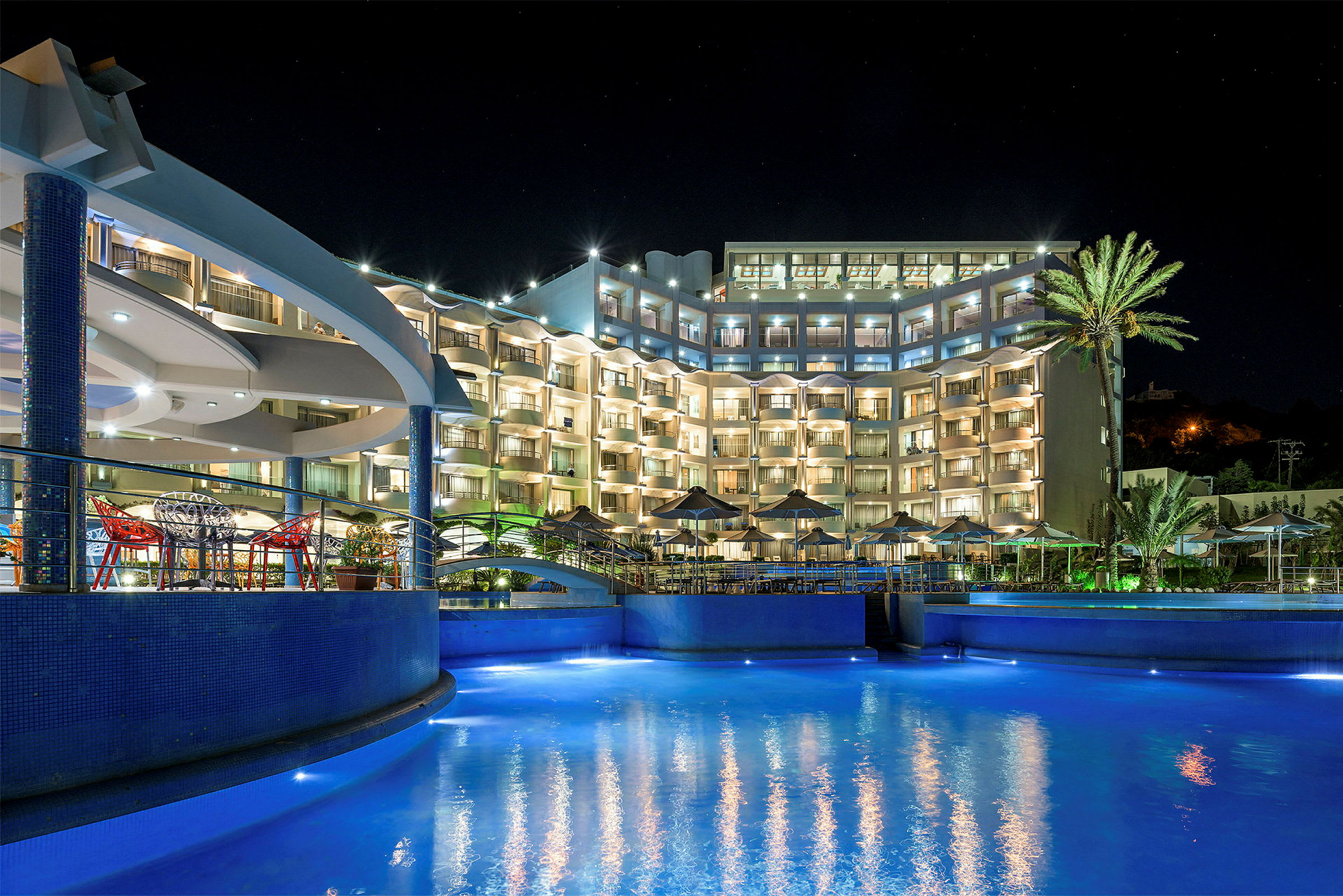 Hotellbyggnad med upplysta balkonger och en pool i förgrunden på natten. (AI-genererad text)