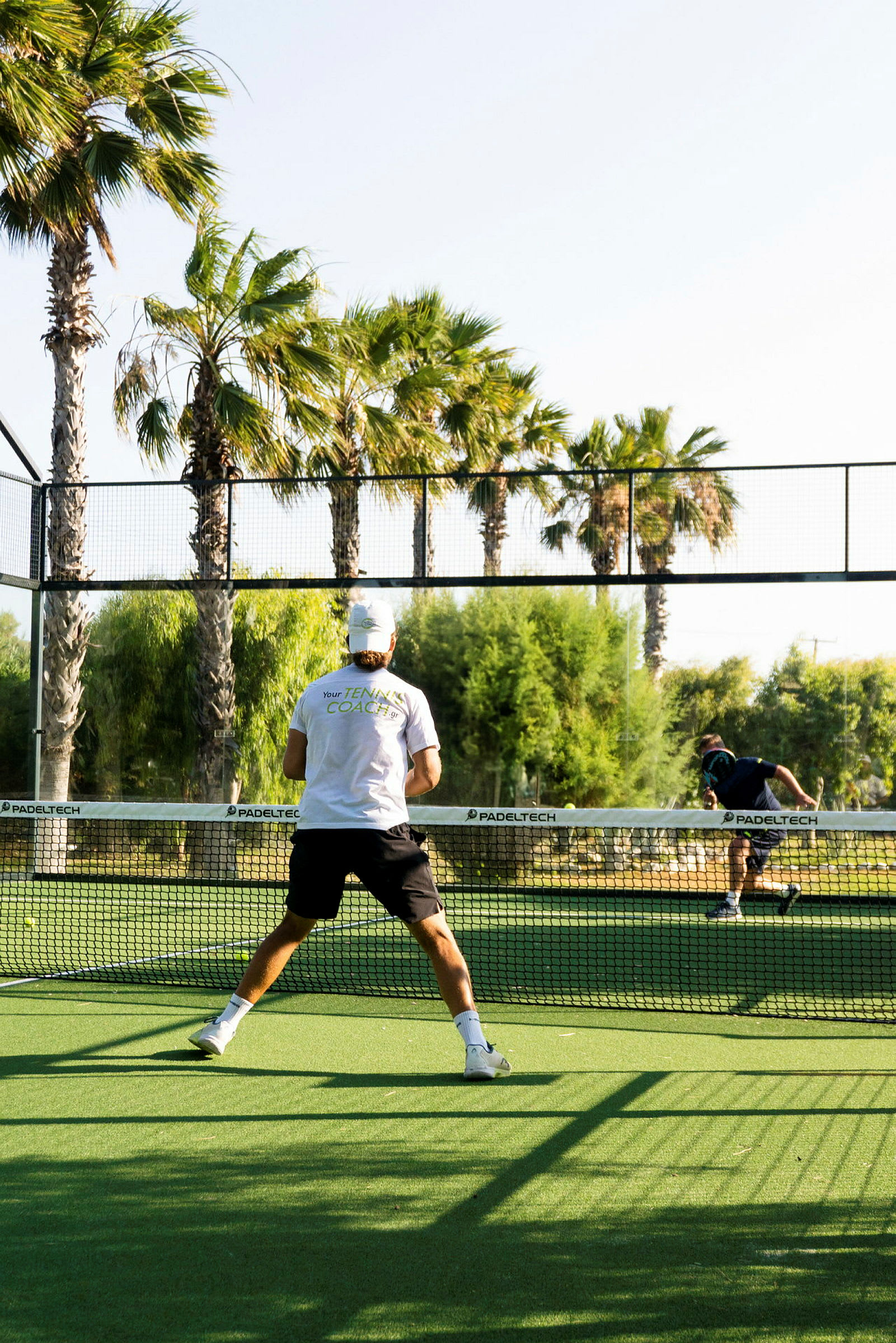 En man spelar padeltennis på en utomhusbana med palmer runtomkring. (AI-genererad text)