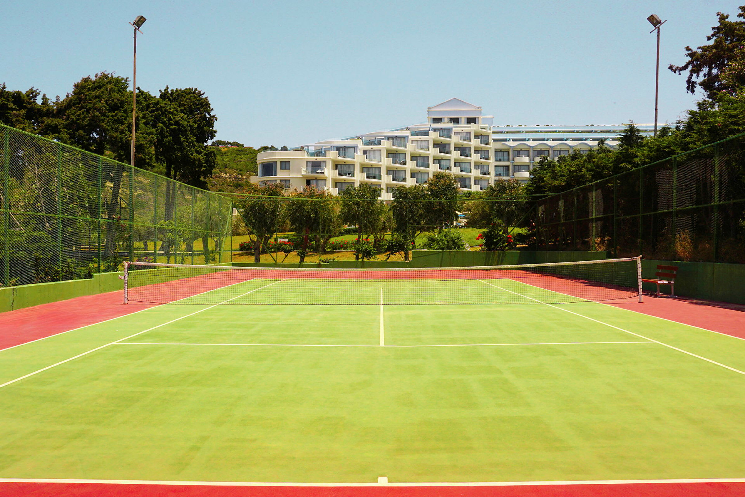En grön tennisbana med ett nät i mitten och ett hotell i bakgrunden omgivet av träd. (AI-genererad text)