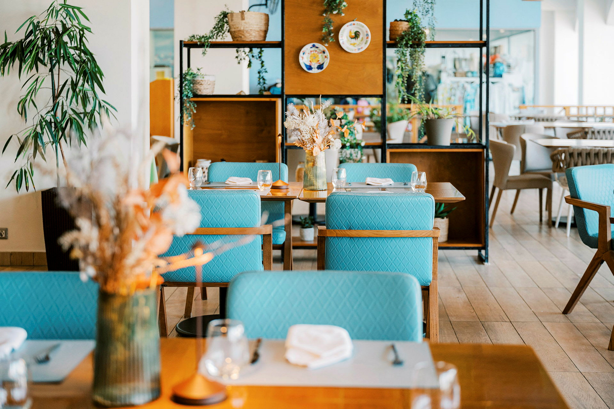 Ett modernt inrett restaurangområde med bord, turkosa stolar och dekorativa växter. (AI-genererad text)
