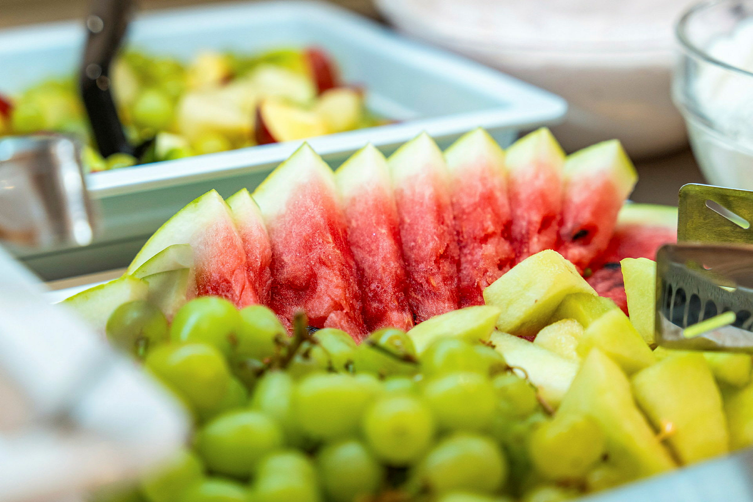 Bitar av färsk vattenmelon, vindruvor och ananas ligger upplagt på ett serveringsfat. (AI-genererad text)