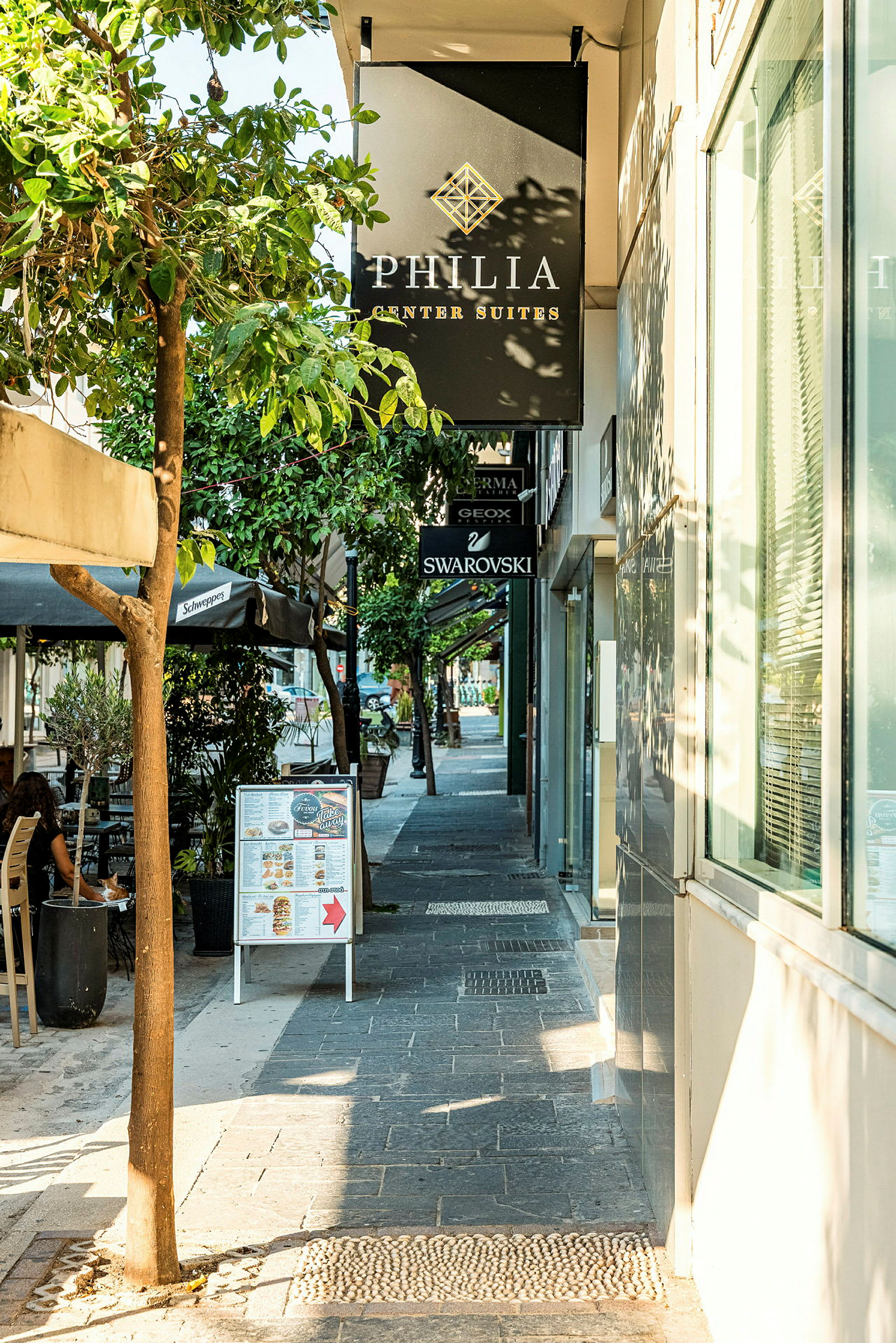 Gata med butiker och restauranger, träd och skyltar längs trottoaren. (AI-genererad text)
